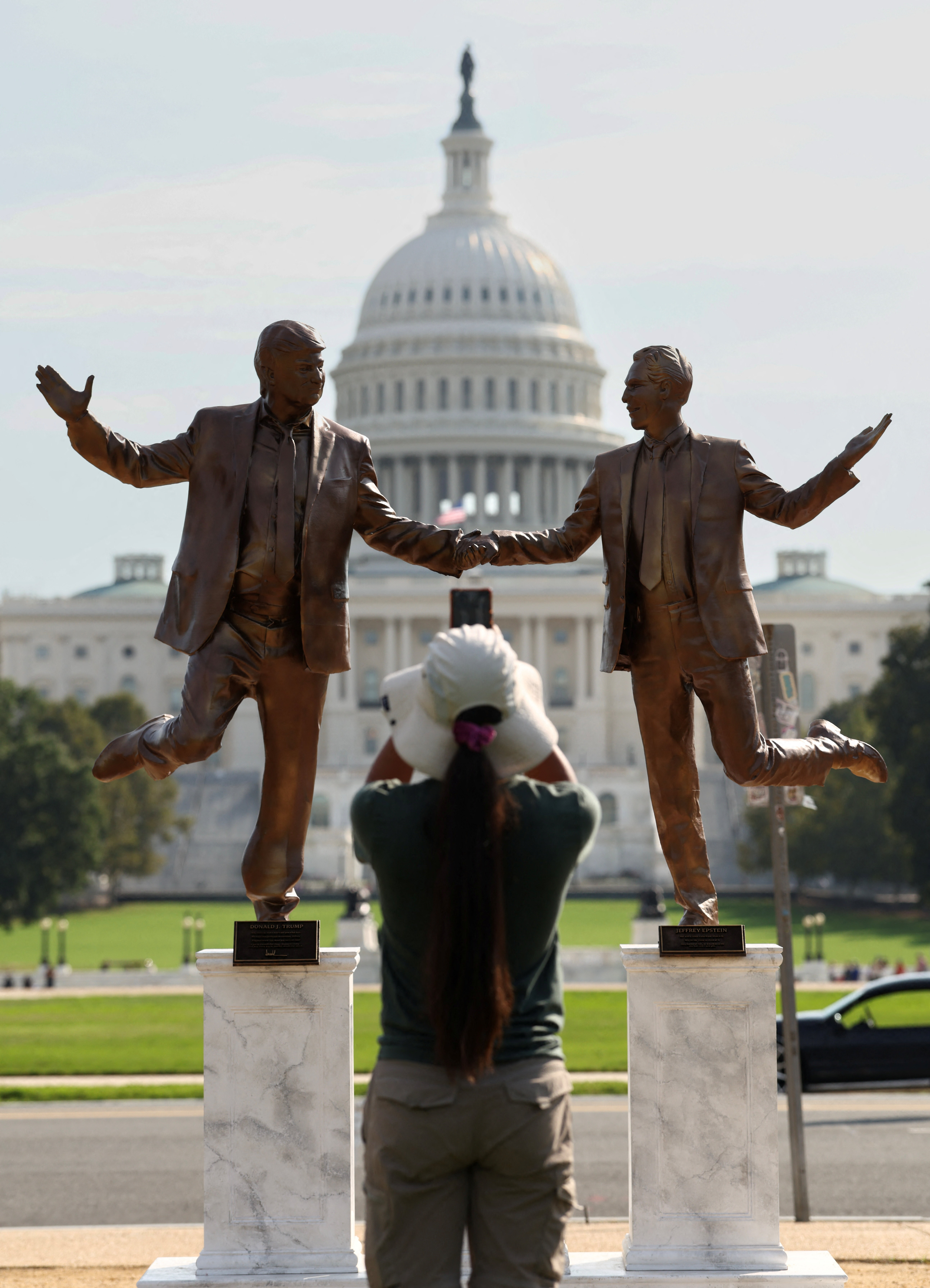 A woman takes a photo of a pop-up statue depicting U.S. President Donald Trump and disgraced financier and sex offender Jeffrey Epstein dancing together near the U.S. Capitol in Washington, D.C., U.S., September 23, 2025. REUTERS/Kevin Lamarque