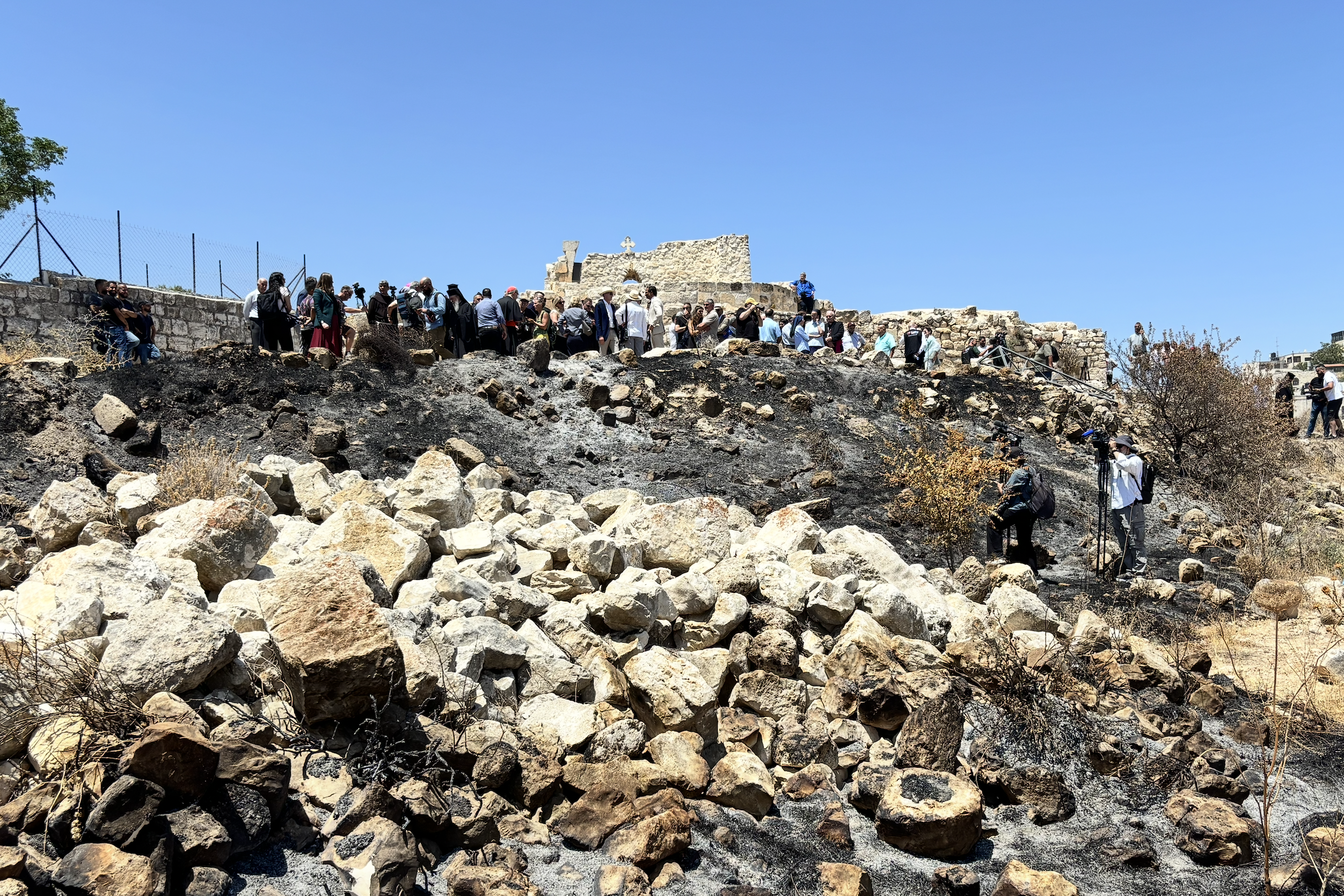 Charred material next to rocks at the bottom of a hill, with a structure at the top of the hill