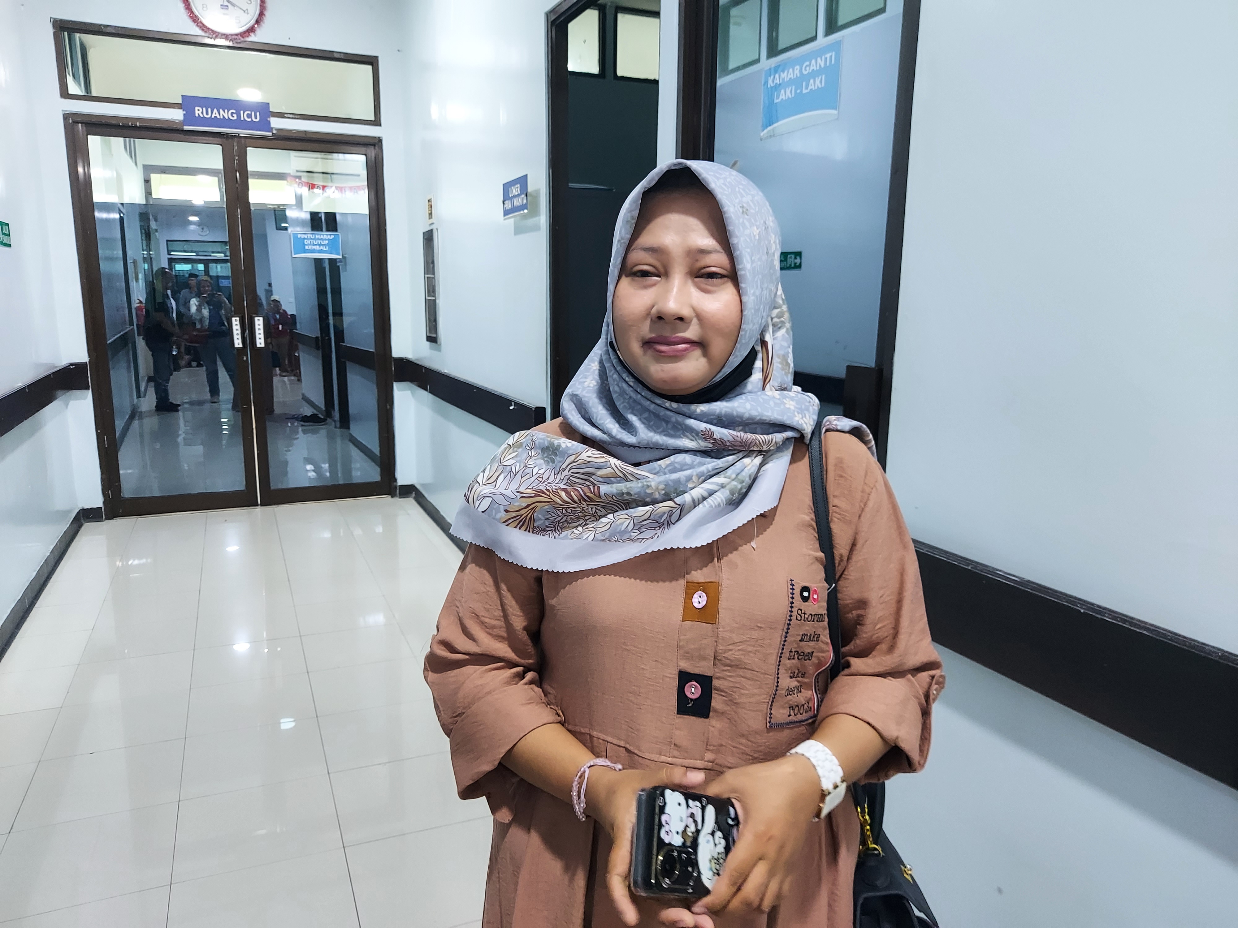 416: Dewi Ajeng stands in front of the intensive care unit at Sidoarjo Hospital where her son Haikal is receiving treatment.