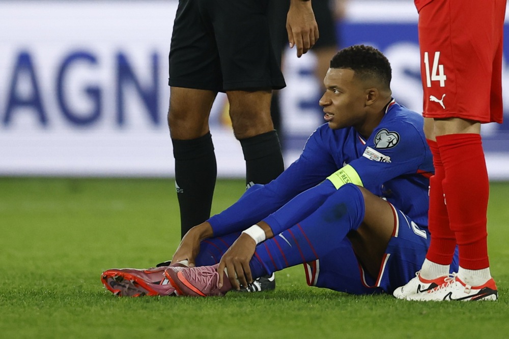 Kylian Mbappe of France looks on as he sits on the ground.