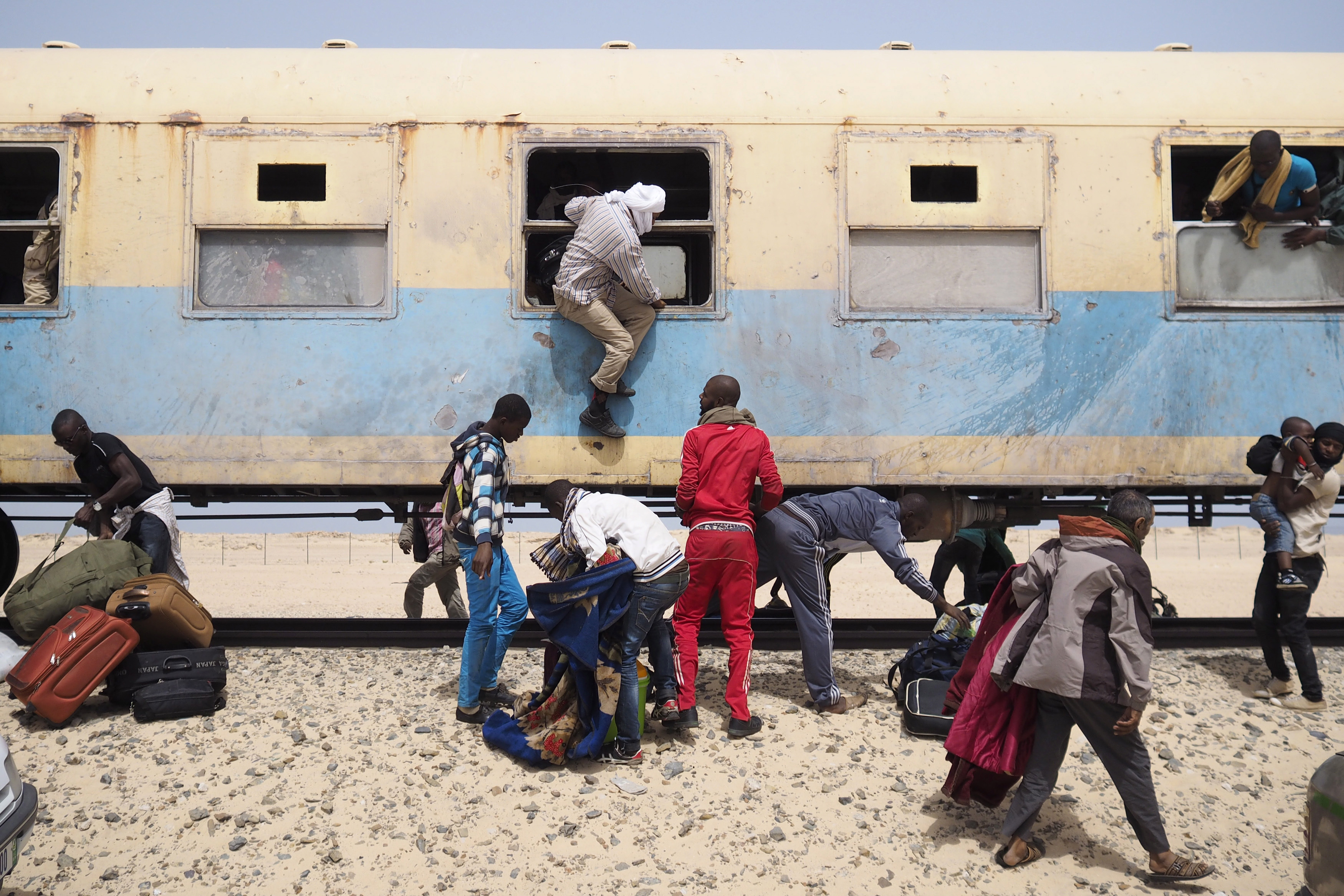 Passengers disembark from a train onto a sandy road.