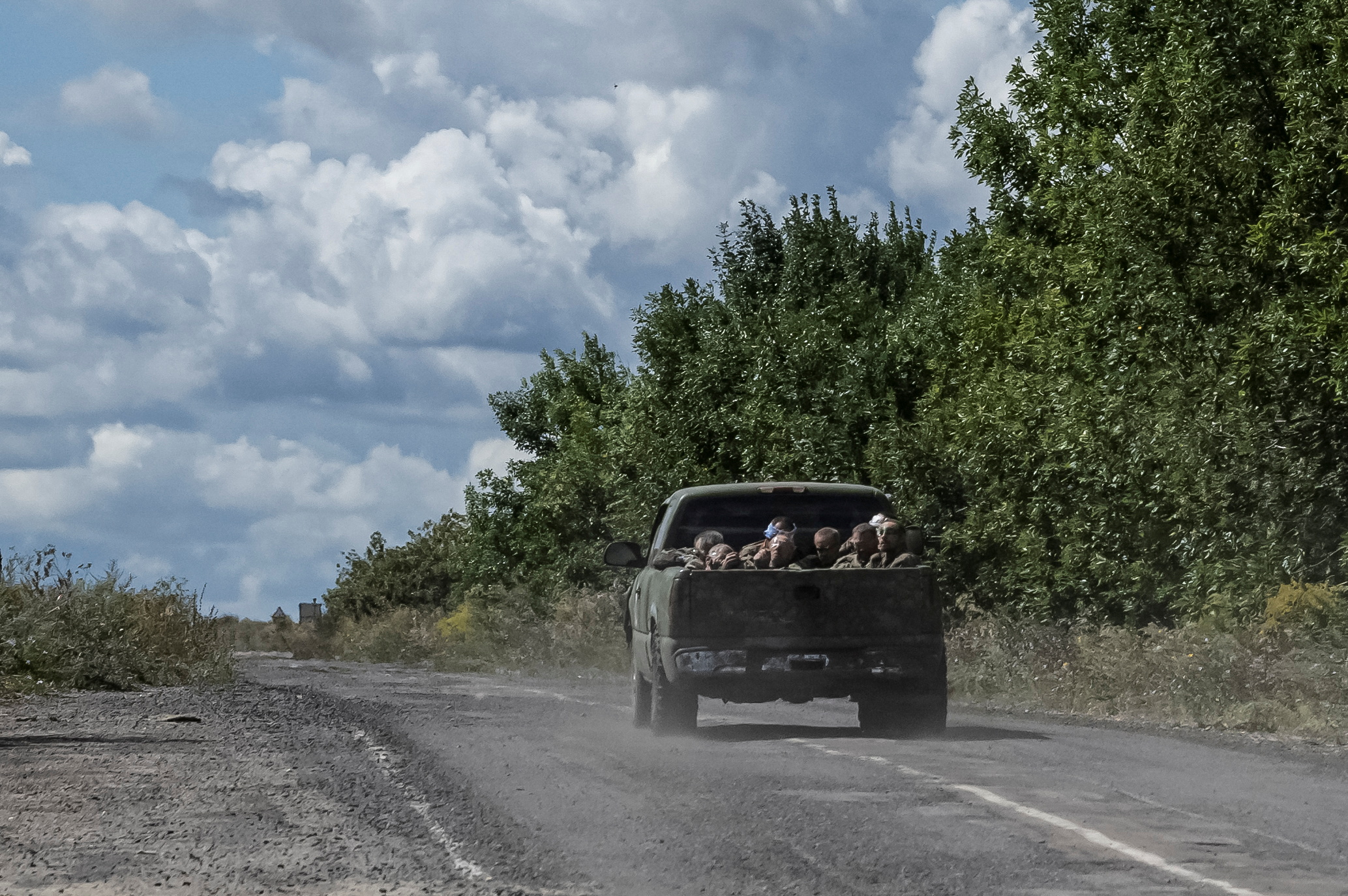 Ukrainian soldiers ride a military vehicle with Russian POWs in the truck bed.