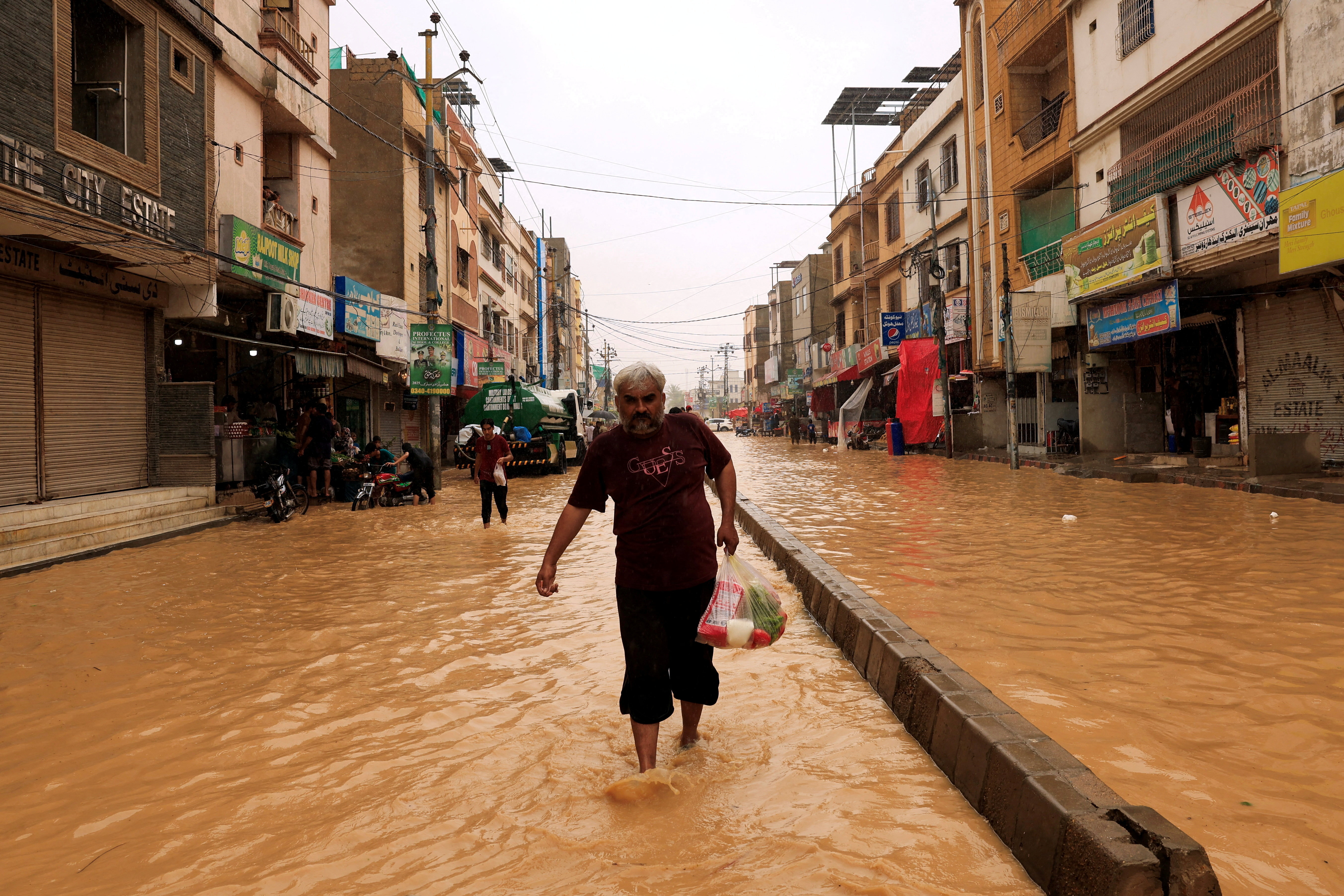 A resident carries a bag of groceries as he wades through a flooded street.