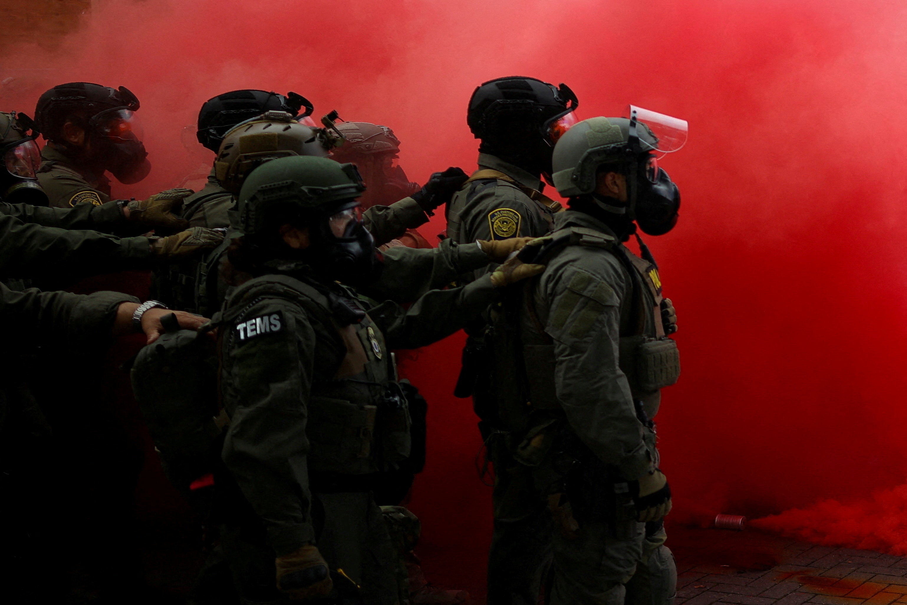 Law enforcement officers stand amid smoke from a smoke grenade released to disperse demonstrators in front of U.S. Immigration and Customs Enforcement (ICE) headquarters in Portland, Oregon, U.S
