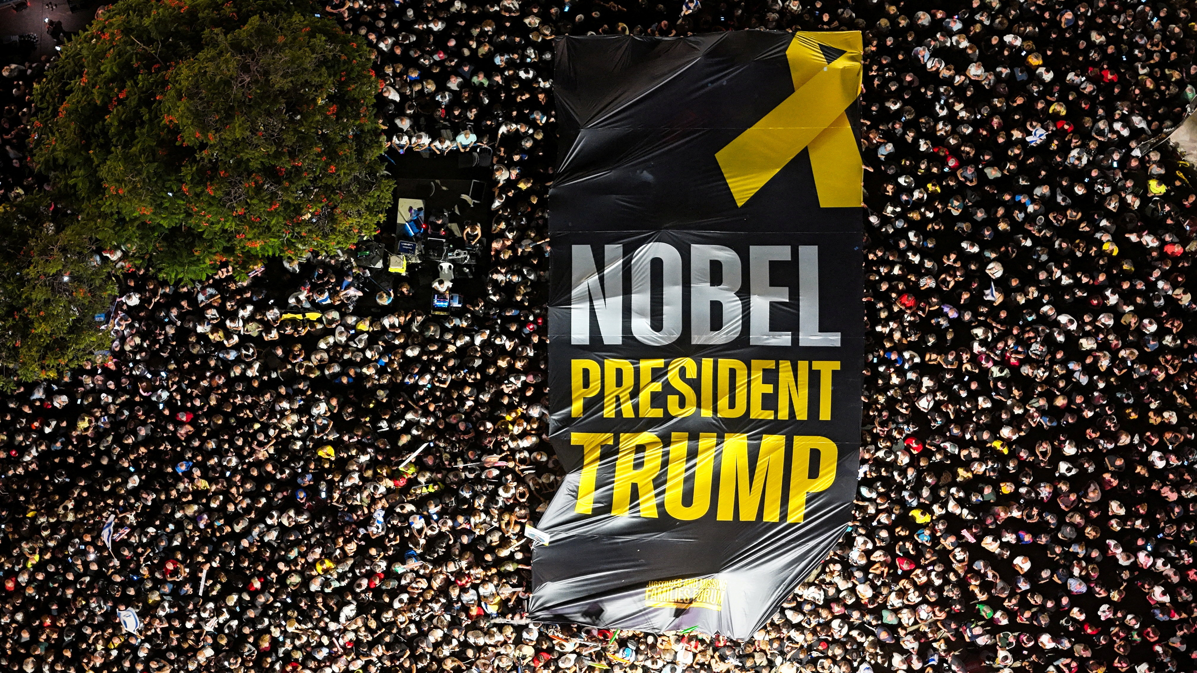 A drone photo of people gathering in "Hostages square" as they hold up a giant sign with the words "NOBEL PRESIDENT TRUMP"