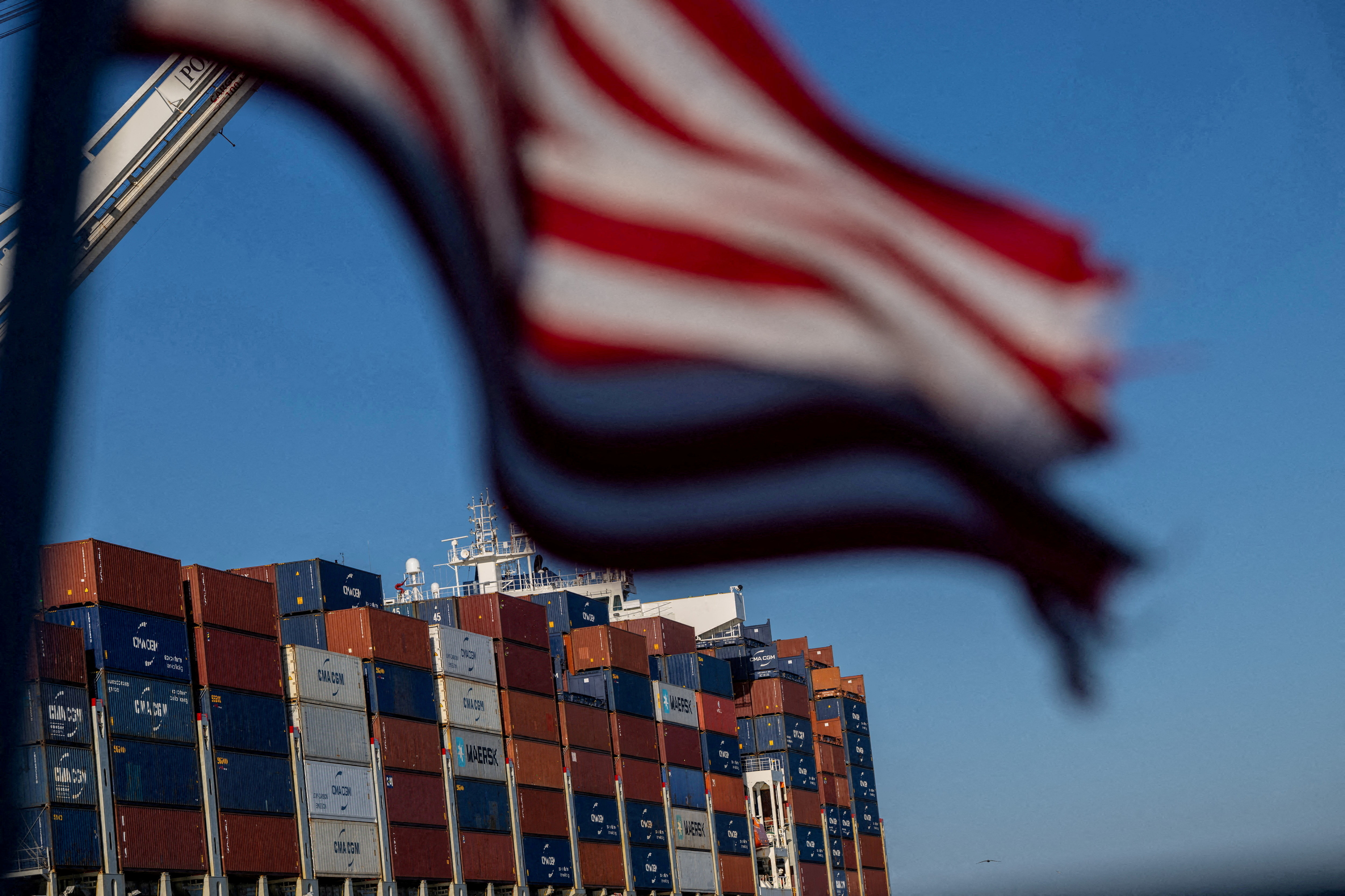 A US flag waves in front of containers on a container ship.