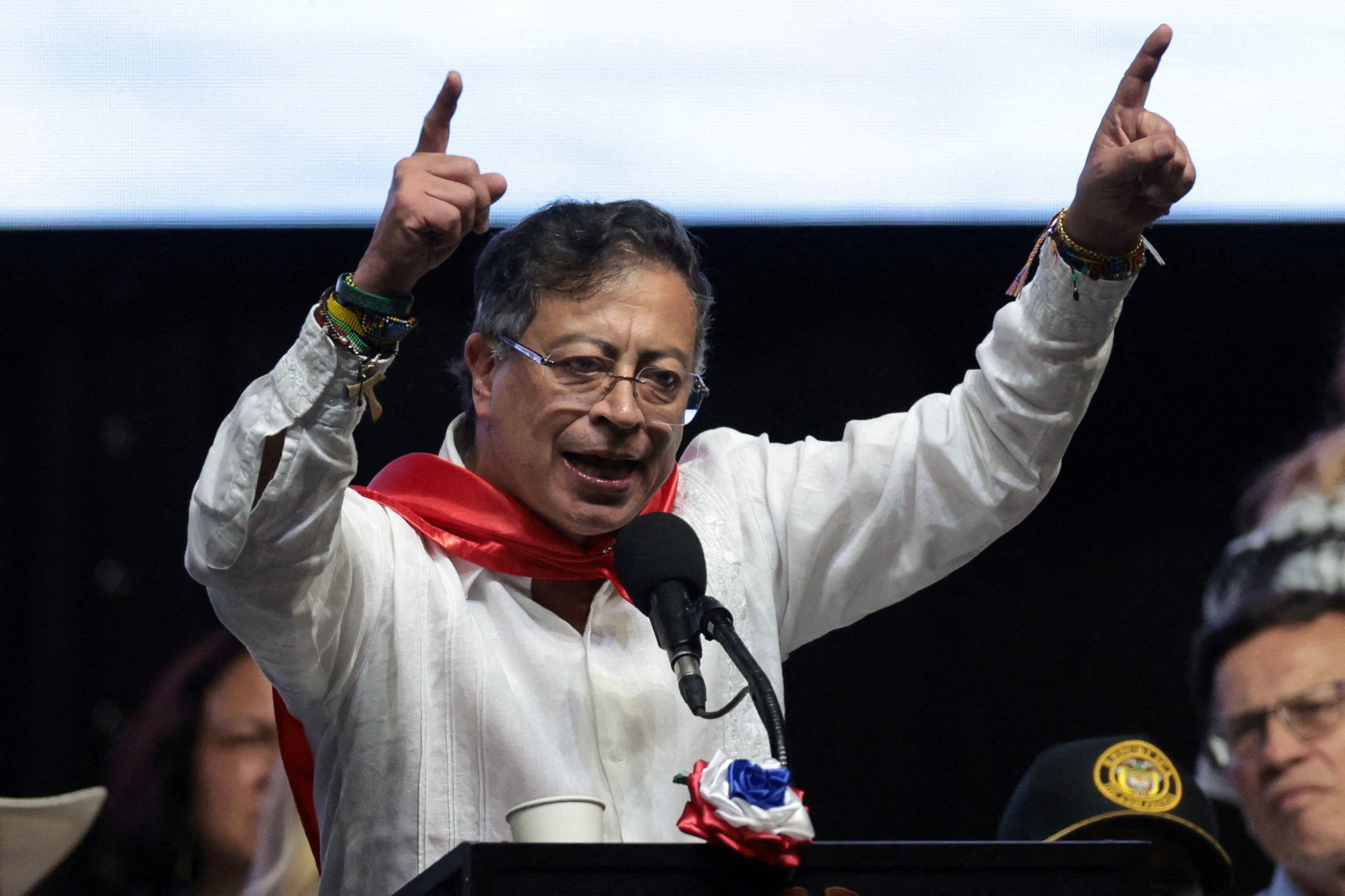 Gustavo Petro, wearing a red scarf and lifting his arms to point at the sky