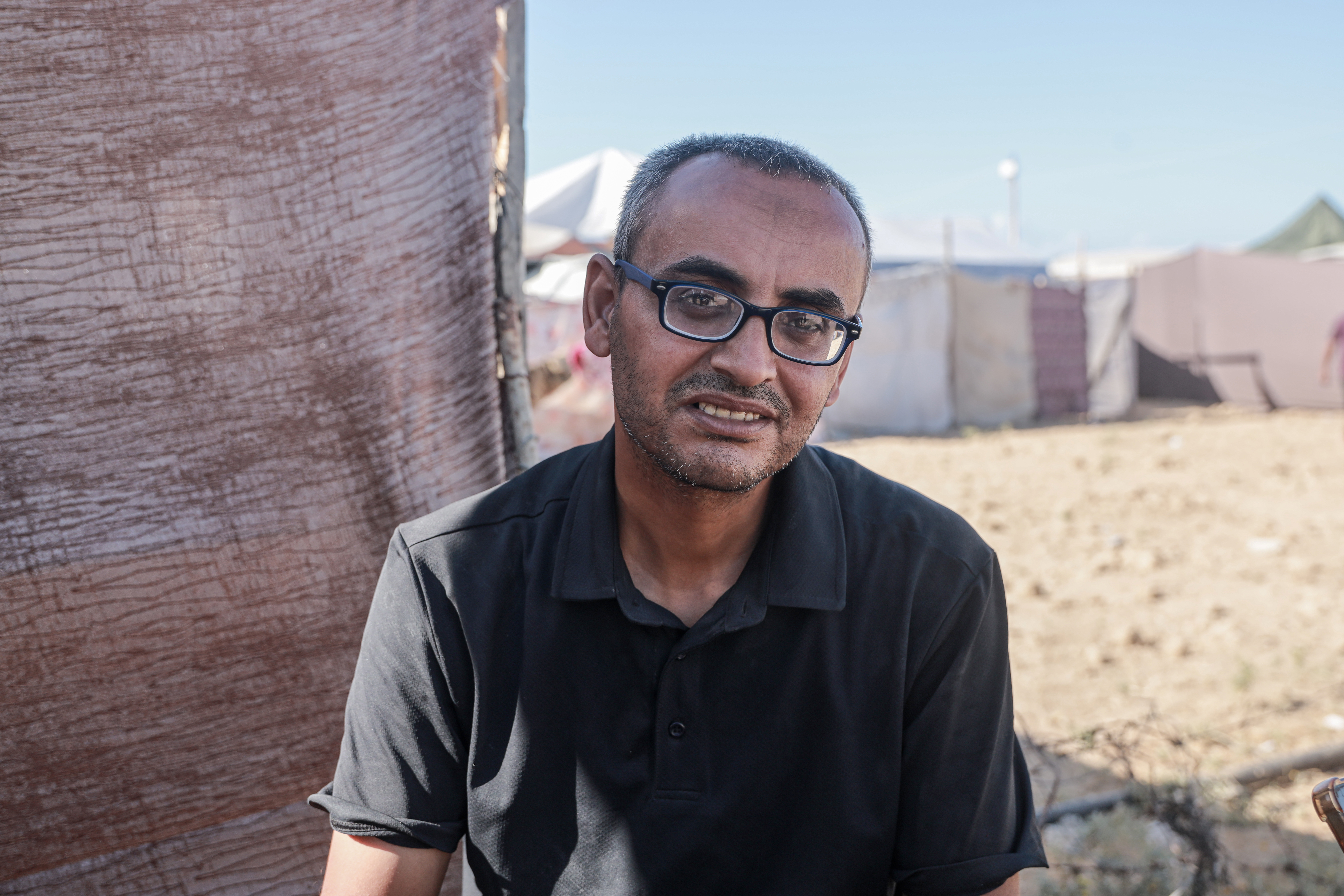 An emaciated man wearing glasses and a t-shirt that now bags on him