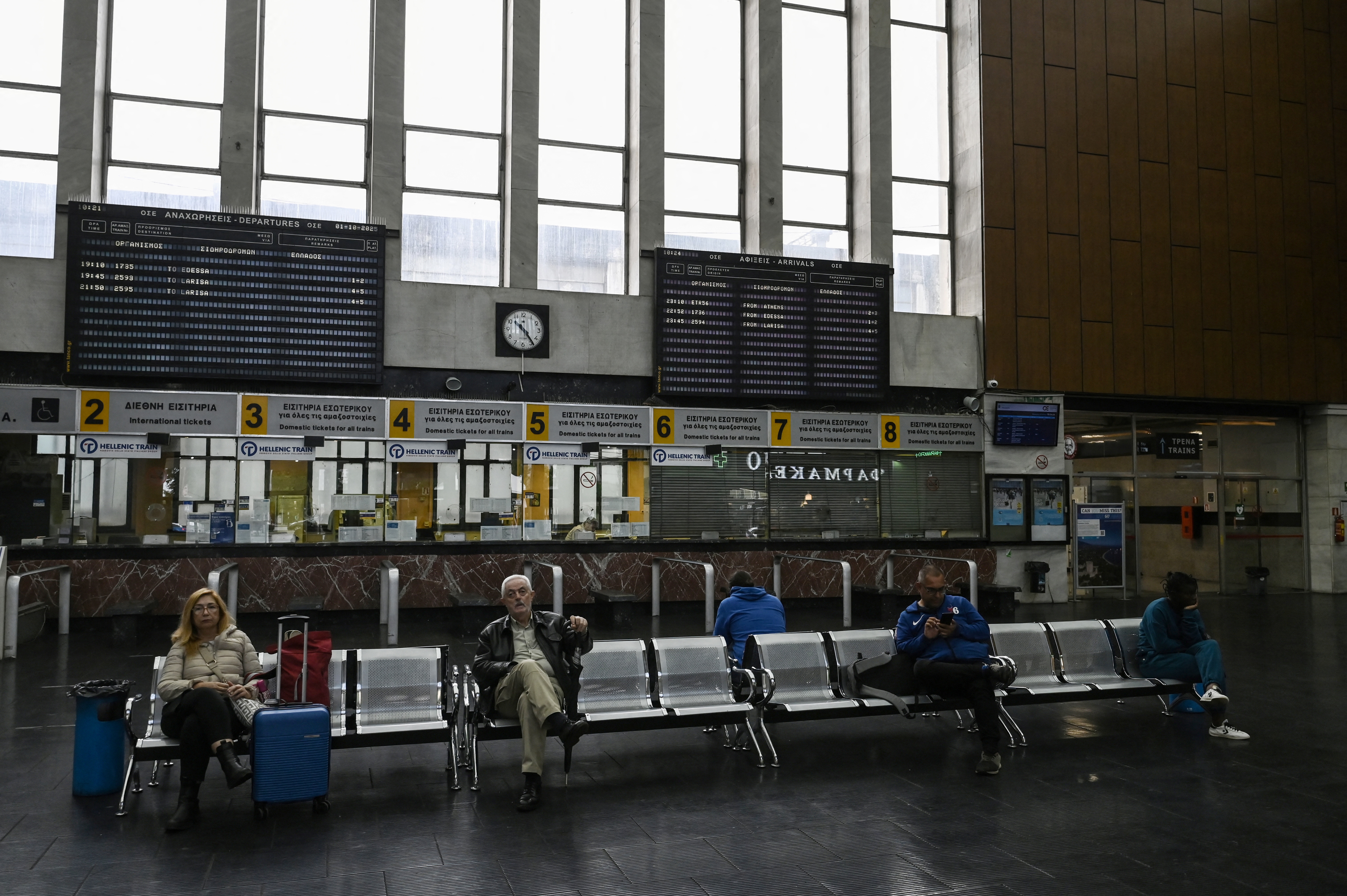 People sit in a train station during a 24-hour general strike, in Thessaloniki on October 1, 2025. Greece will grind to a halt on Ocotober 1, 2025 in a 24-hour general strike against plans by the conservative government to introduce a 13-hour workday.Transport in Athens, trains and ferry services will be disrupted while teachers, hospital staff, and civil servants are also taking part in the mobilization. (Photo by Sakis Mitrolidis / AFP)