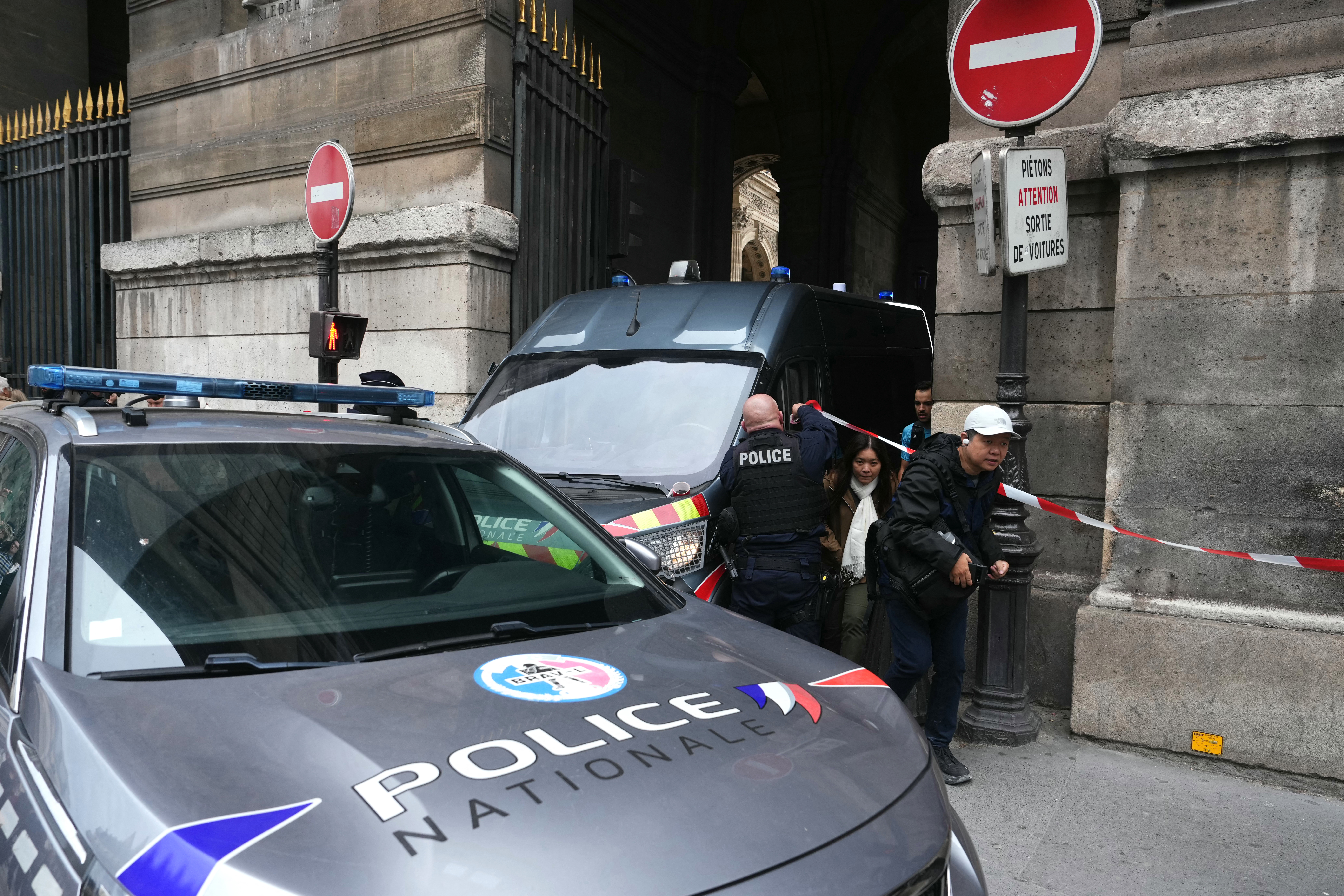 Tourists walk past a French police officer after the Louvre Museum was closed following a robbery, in Paris on October 19, 2025