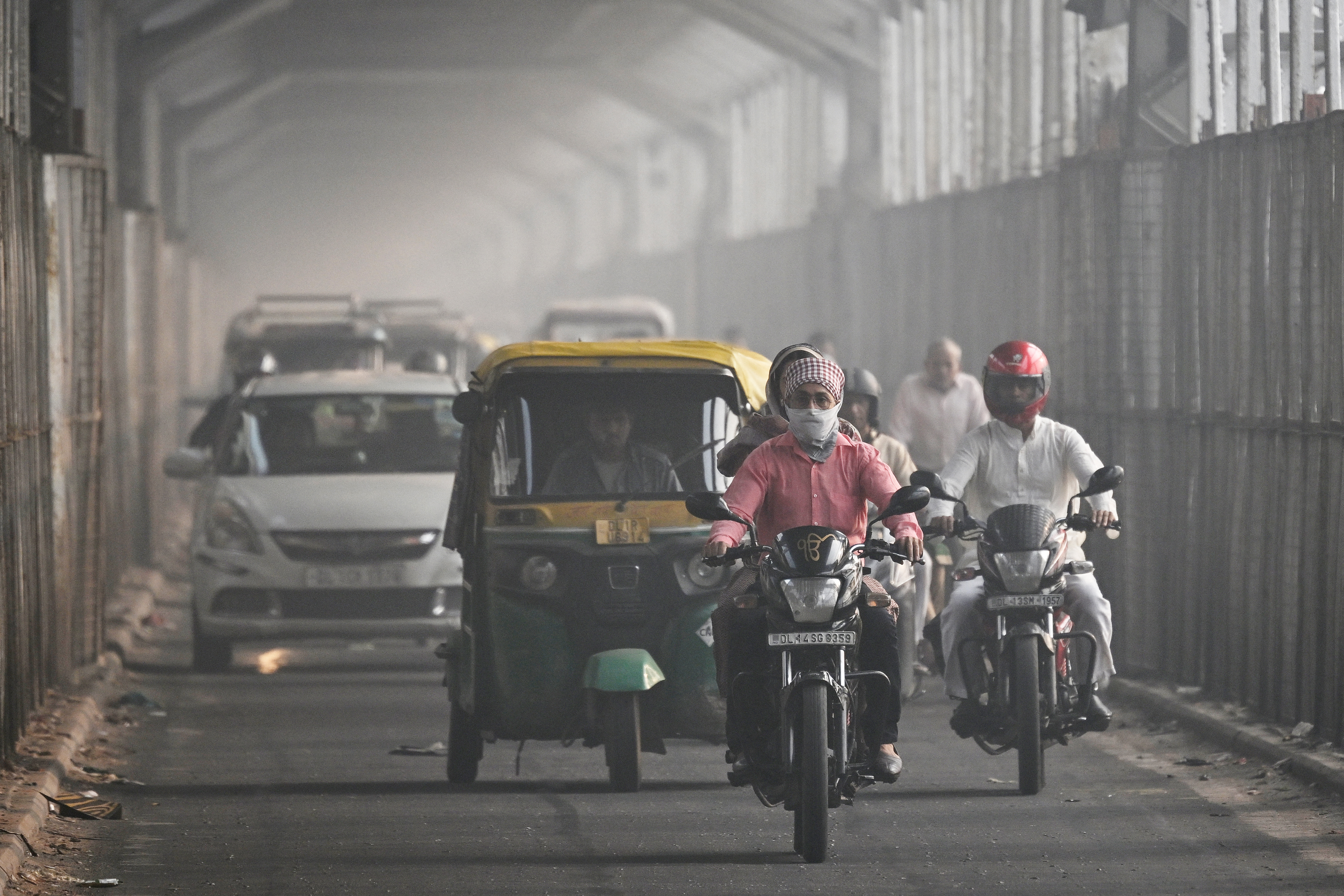 A commuter with his face covered in cloth rides along a bridge across river Yamuna in New Delhi on October 21, 2025, as smog engulfed the city skyline a day after Diwali, the Hindu festival of lights. Toxic air in India's capital spiralled to more than 23 times UN daily health limits on October 21, as the annual winter pollution blanketed the sprawling urban area of 30 million people. (Photo by Arun SANKAR / AFP)