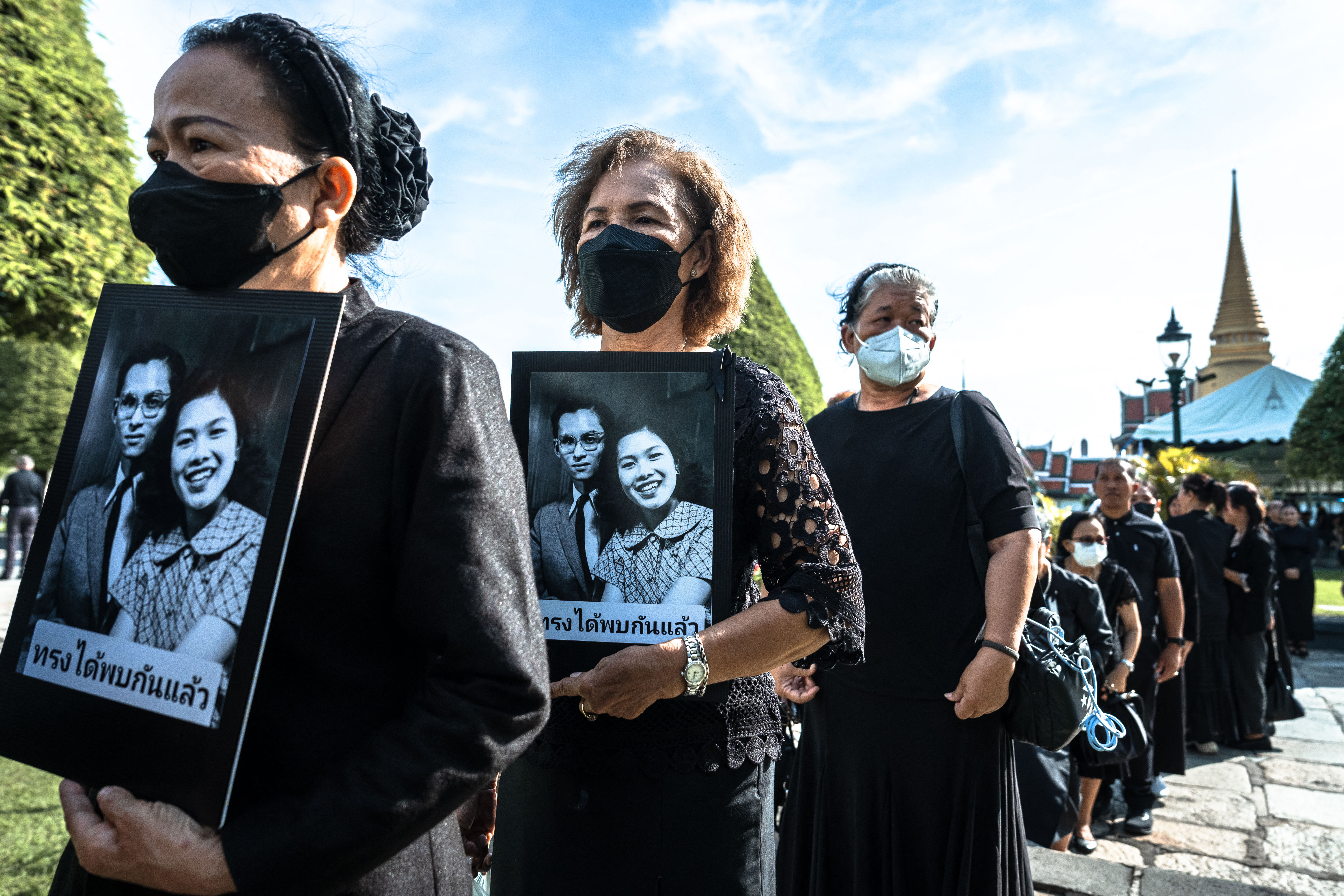 Mourners hold portraits of Thailand's former Queen Sirikit and King Bhumibol Adulyadej as they line up to pay respects to the late queen at the Grand Palace in Bangkok