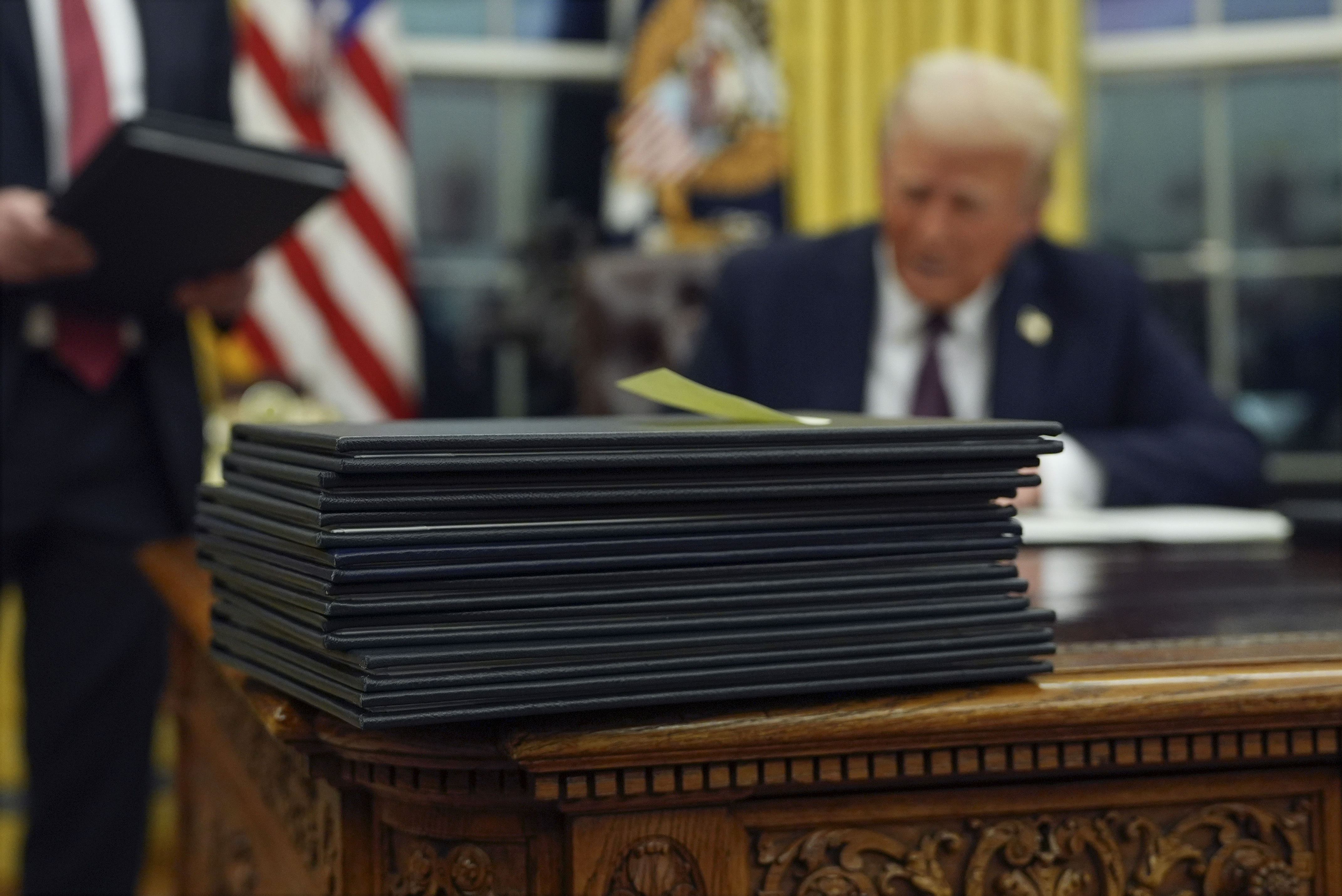 A stack of executive orders as Trump sits at Resolute Desk