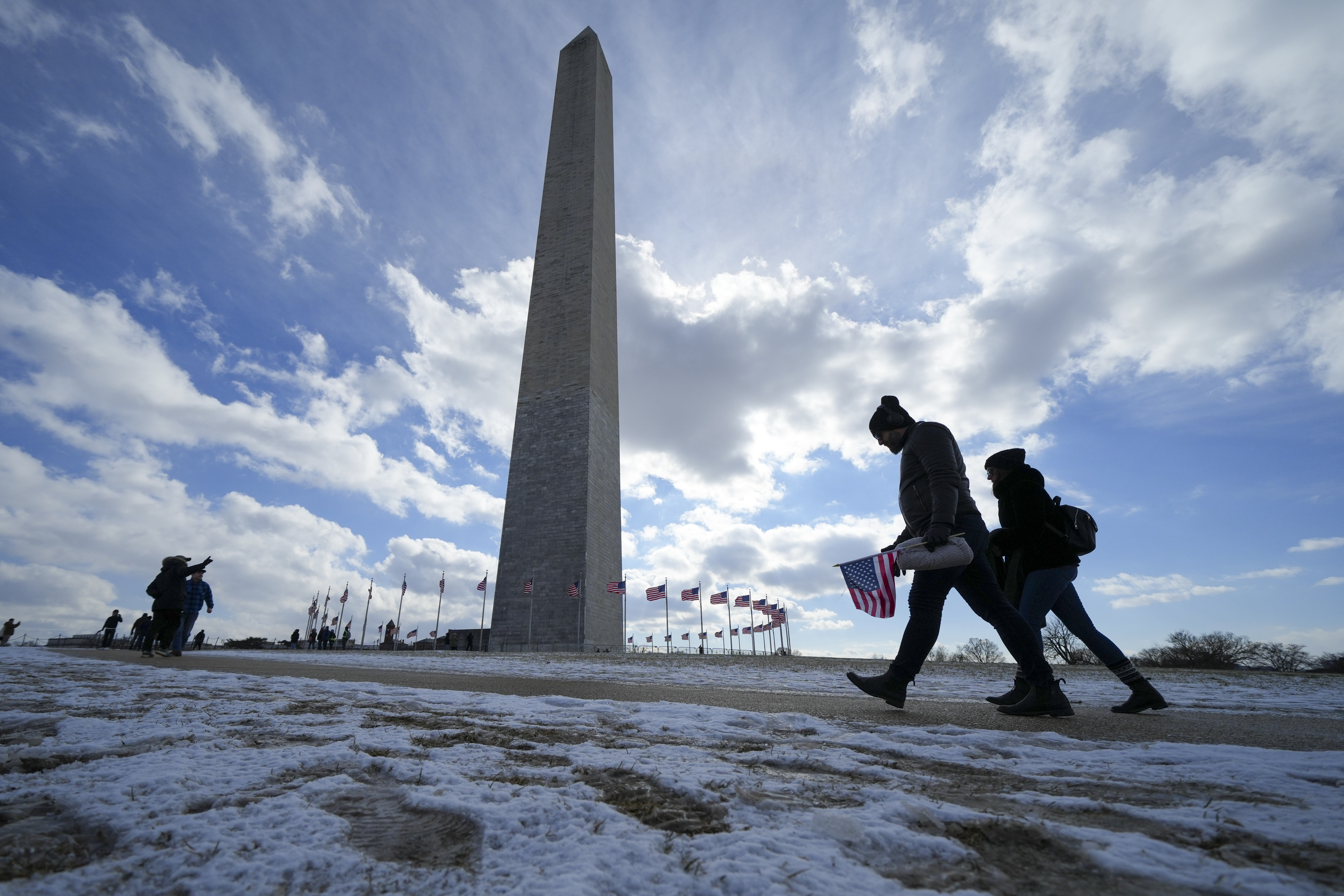 People walk through snow and ice in front of the Washington Monument.