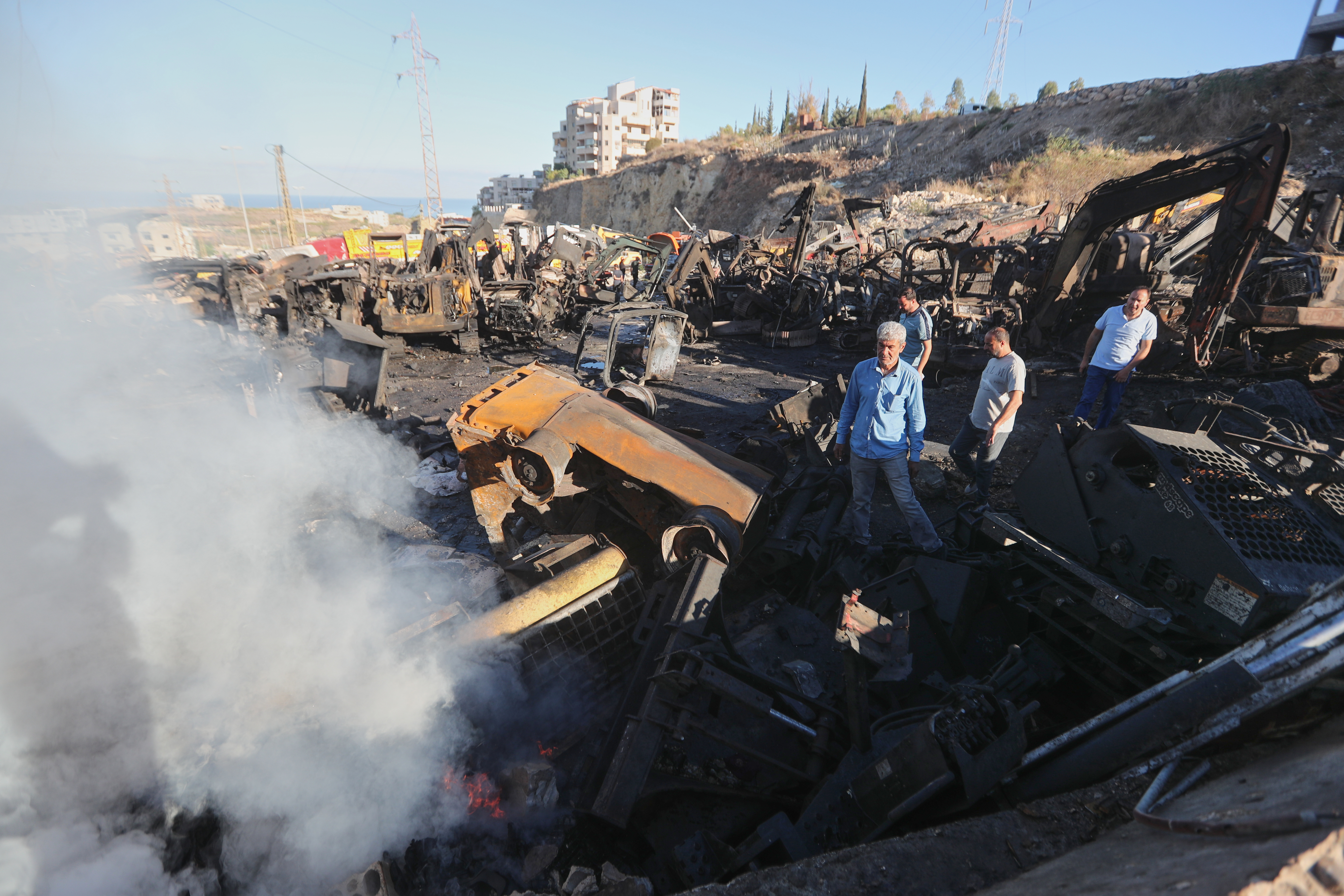 People gather at a site that sold heavy machinery, where a large number of vehicles were destroyed in Israeli airstrikes, in the southern village of Msayleh, Lebanon, Saturday, Oct. 11, 2025. (AP Photo/Mohammed Zaatari)