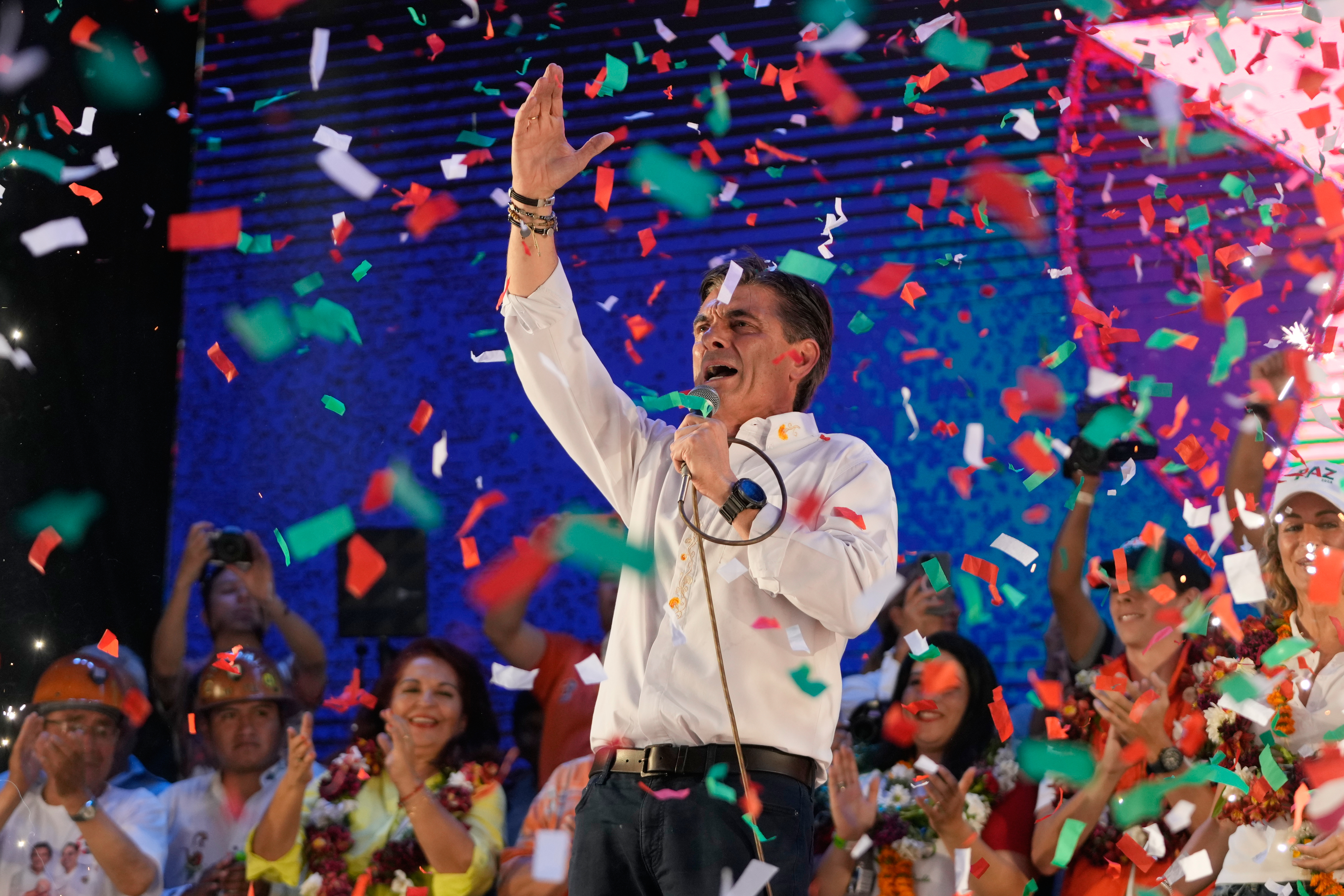 Paz raises an arm and speaks into a microphone during a closing campaign rally in Tarija, Bolivia, as confetti falls.