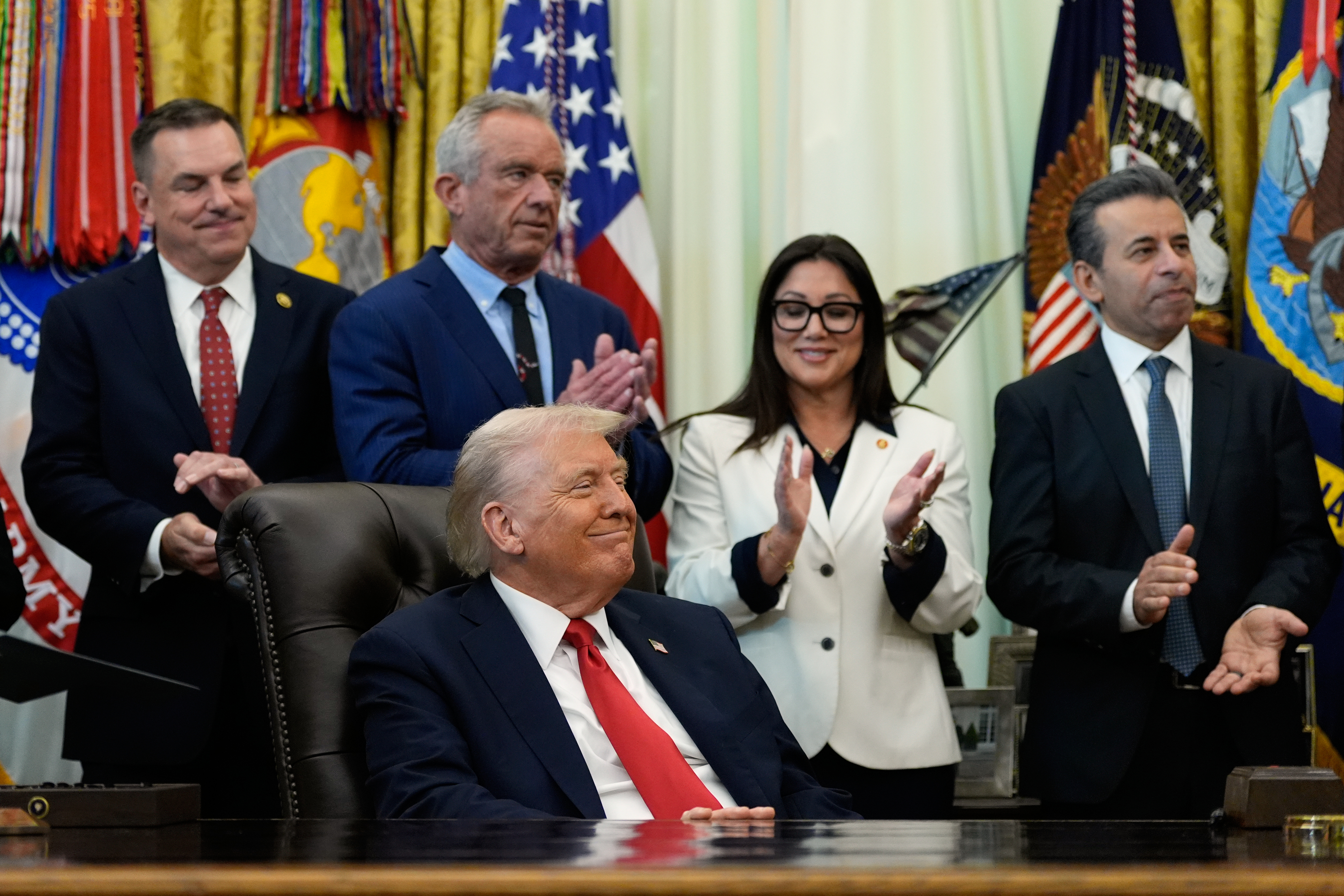 Officials applaud Donald Trump in the Oval Office.