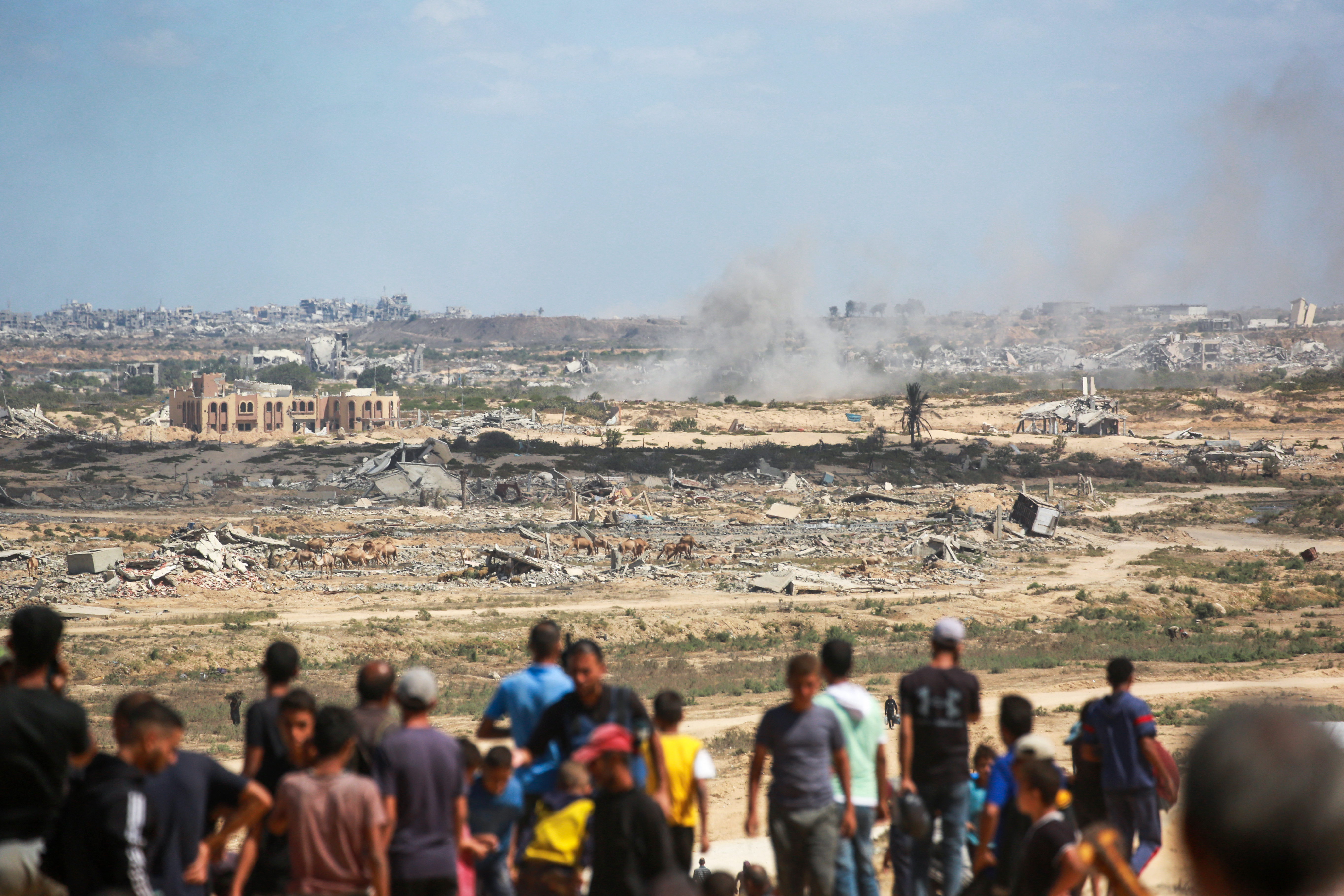 Palestinians watch smoke billowing during Israeli strikes upon arrival on a coastal path northwest of Nuseirat refugee camp as they are displaced southward from Wadi Gaza following an Israeli announcement of closing Al-Rashid road towards the north of the besieged Gaza Strip on October 1, 2025.
