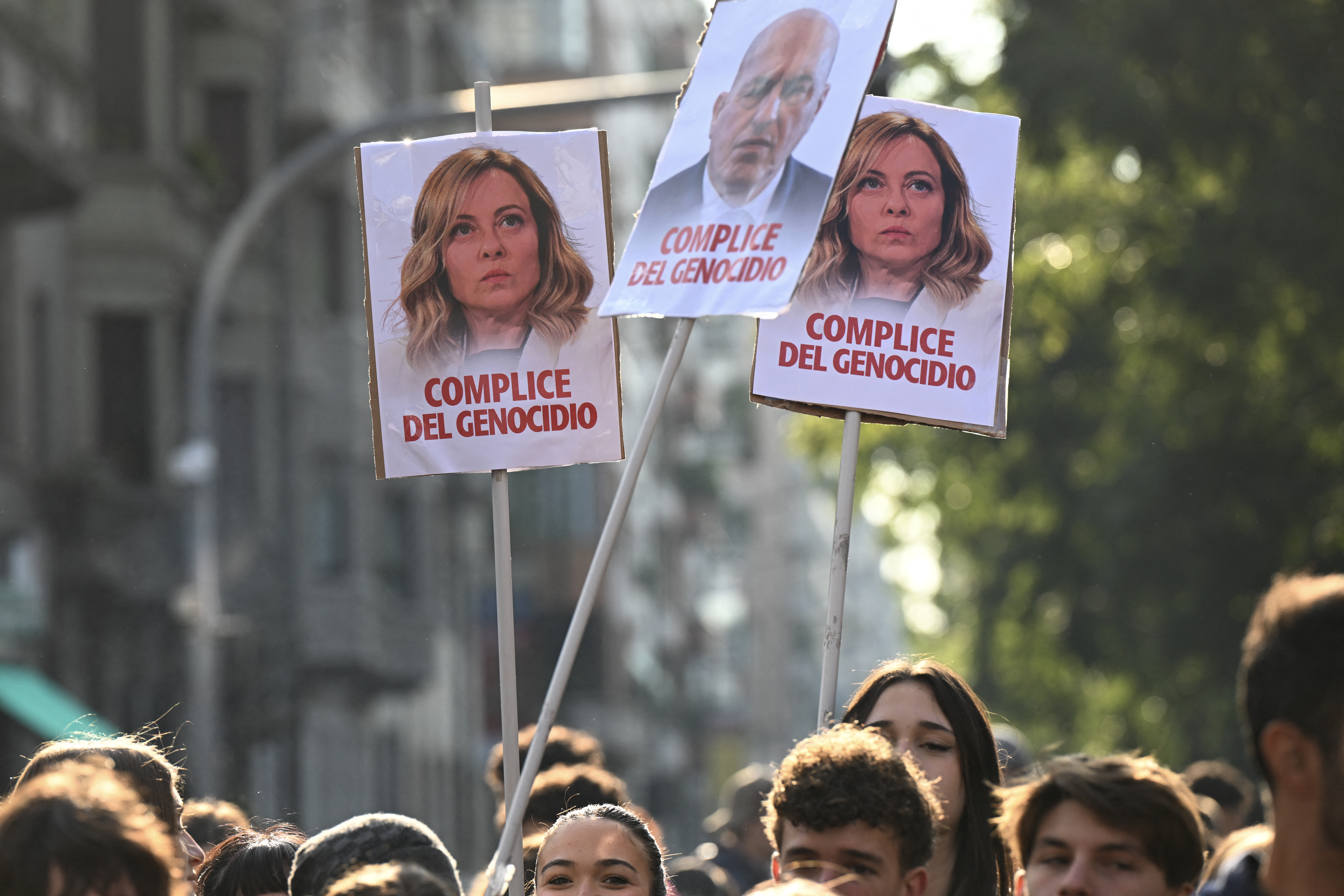 Pro-Palestinian demonstrators hold placards (L and R) depicting Italy's Prime Minister Giorgia Meloni reading "Accomplice to genocide" as they gather to support the Palestinians and to protest against the interception by Israeli army of the Global Sumud Flotilla, in Milan on October 3, 2025. (Photo by Stefano RELLANDINI / AFP)