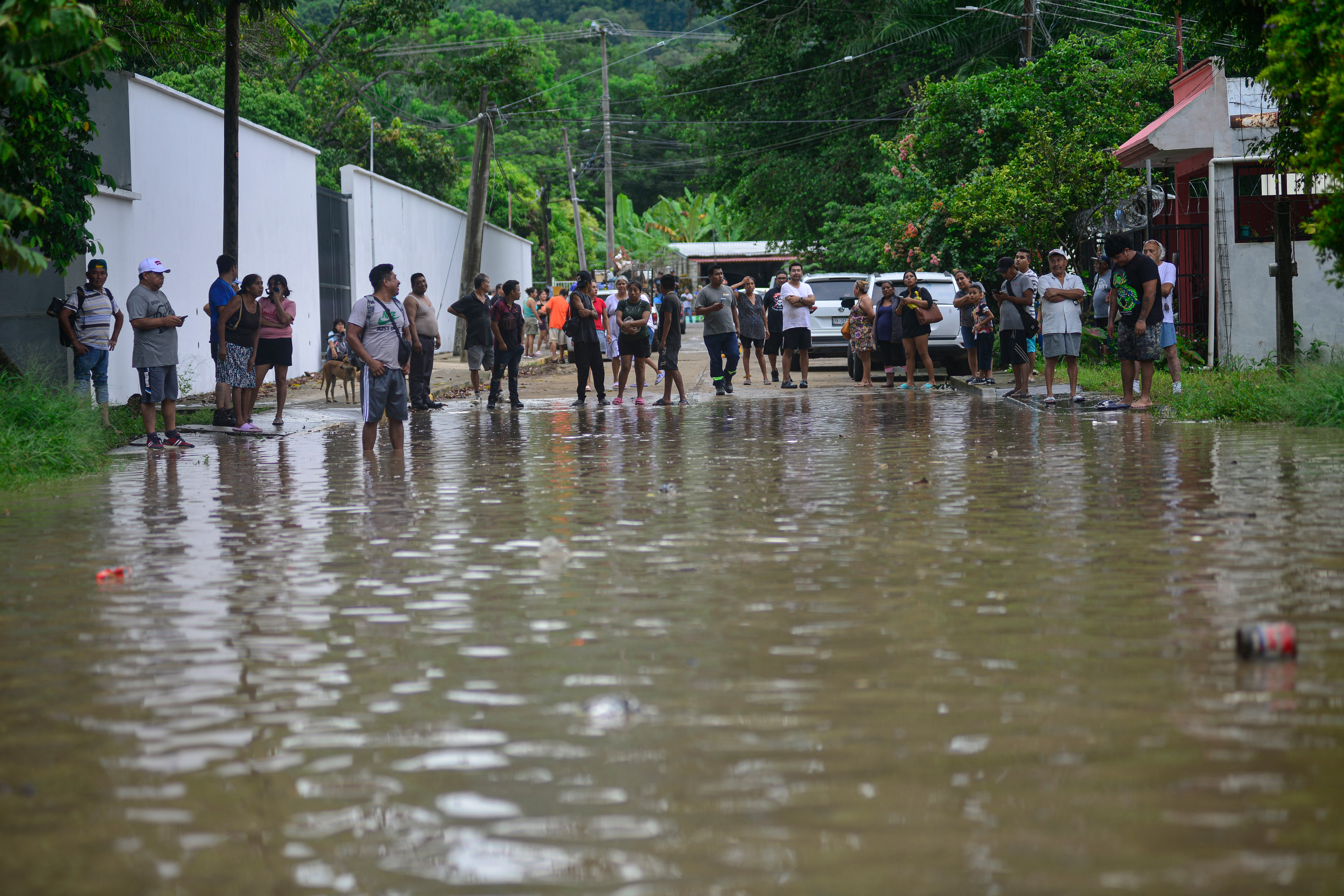 People stand on a flooded street following heavy rains in Poza Rica, Veracruz state, Mexico, on October 10, 2025.