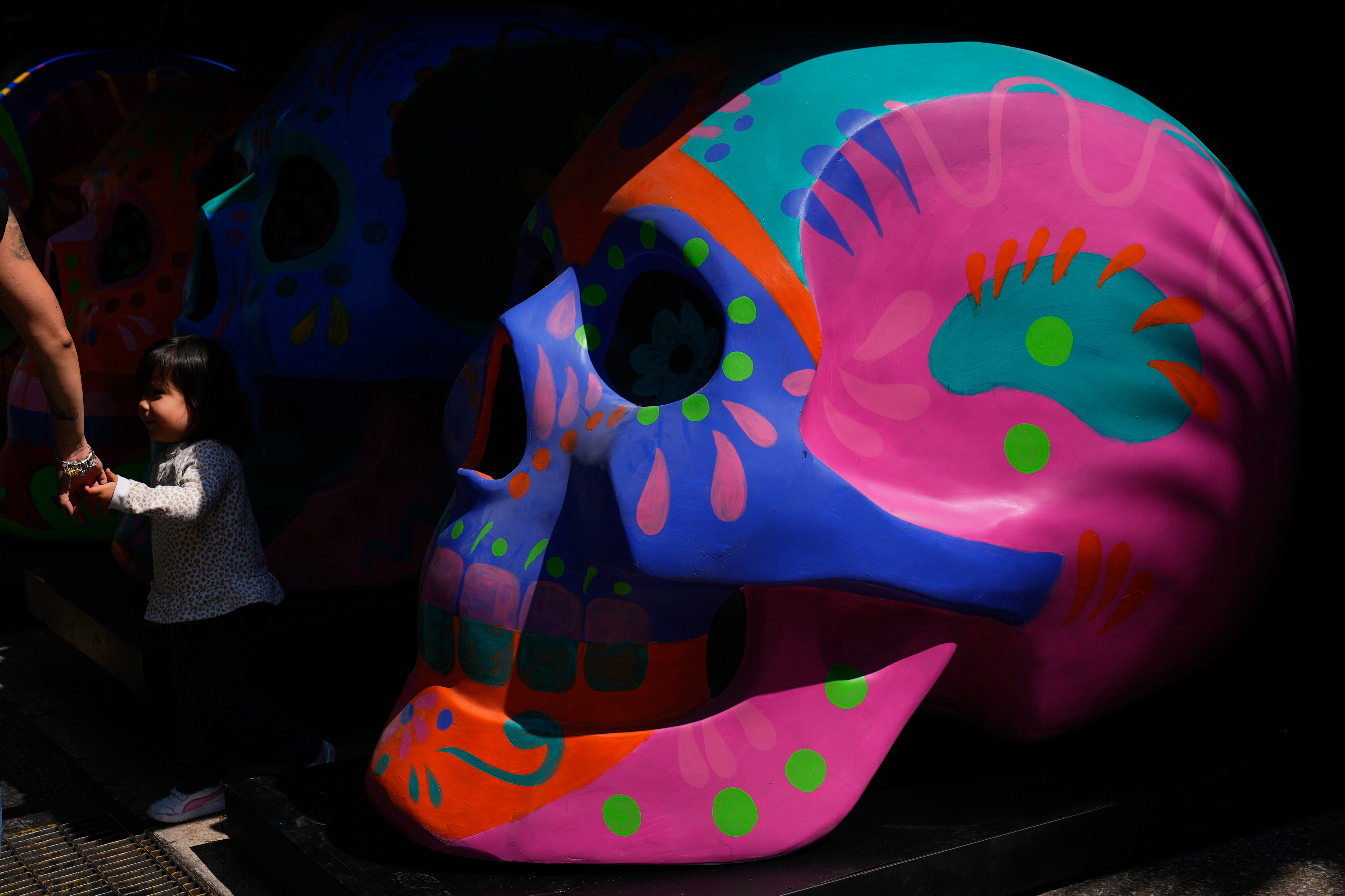 A girl holding her mother’s hand walks past decorative skulls displayed on Reforma Avenue ahead of Day of the Dead festivities in Mexico City, Friday, Oct. 24, 2025. (AP Photo/Marco Ugarte)