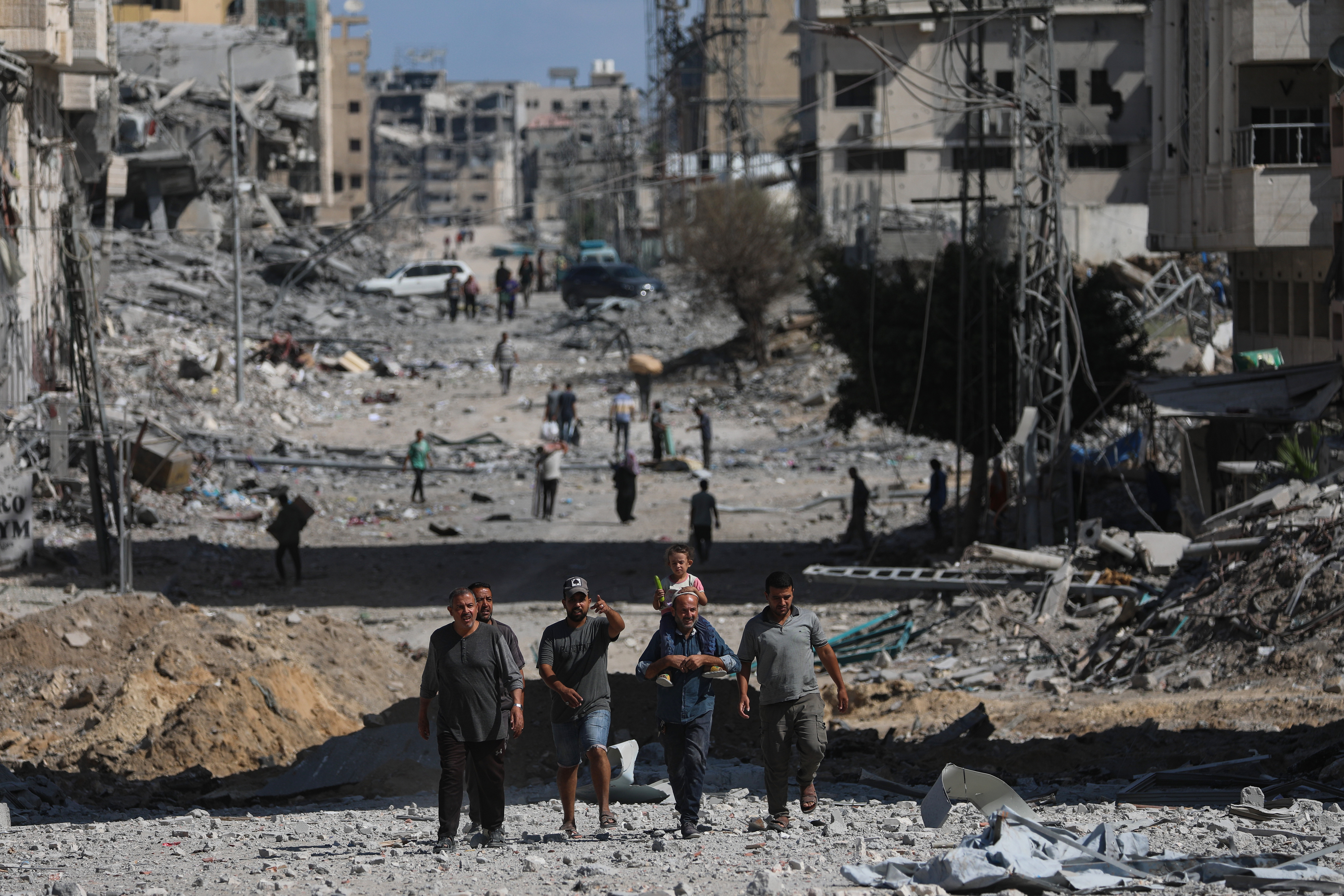 Palestinians walk along a street amid the rubble of destroyed buildings.