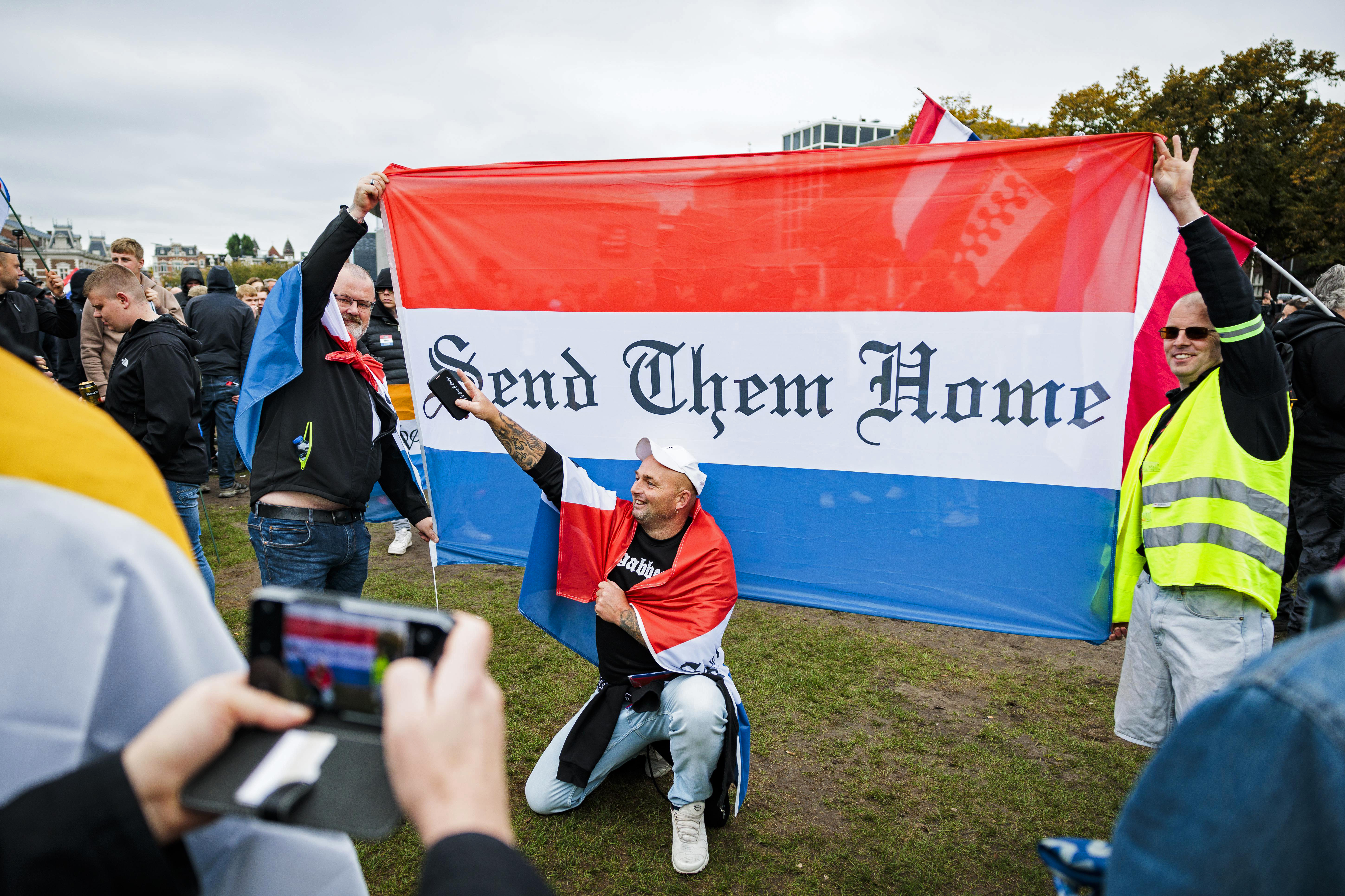 epaselect epa12448356 A person wearing a flag as a cape poses for a photo in front of a banner in the colors of the Dutch flag reading 'send them home' during an anti-immigration rally under the slogan 'against mass immigration, for a safe Netherlands, and against the housing shortage', at Museumplein in Amsterdam, the Netherlands, 12 October 2025. EPA/ROBIN VAN LONKHUIJSEN