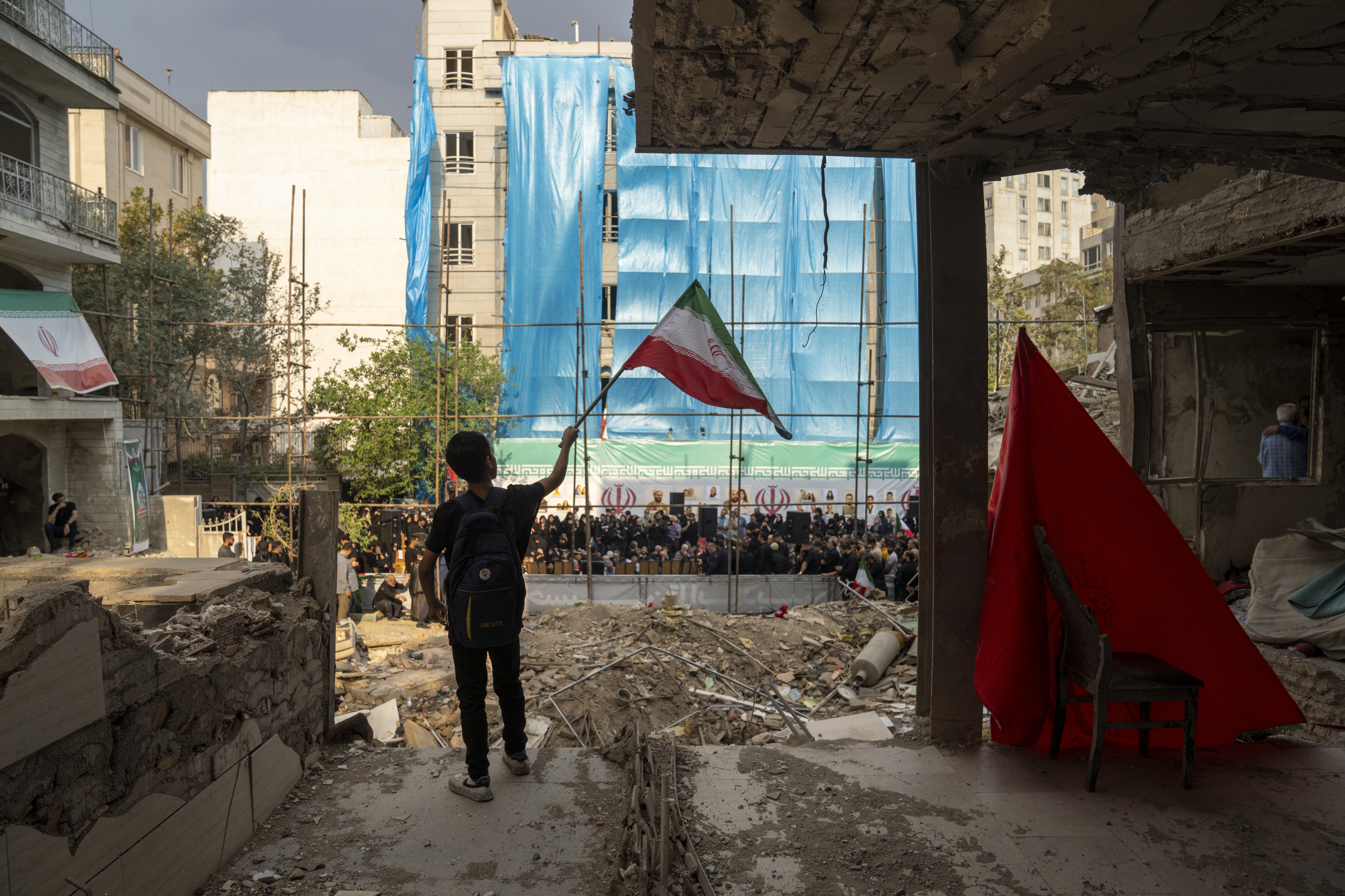 A boy waves an Iranian flag as Iranians gather outside a building hit in Israeli attacks.