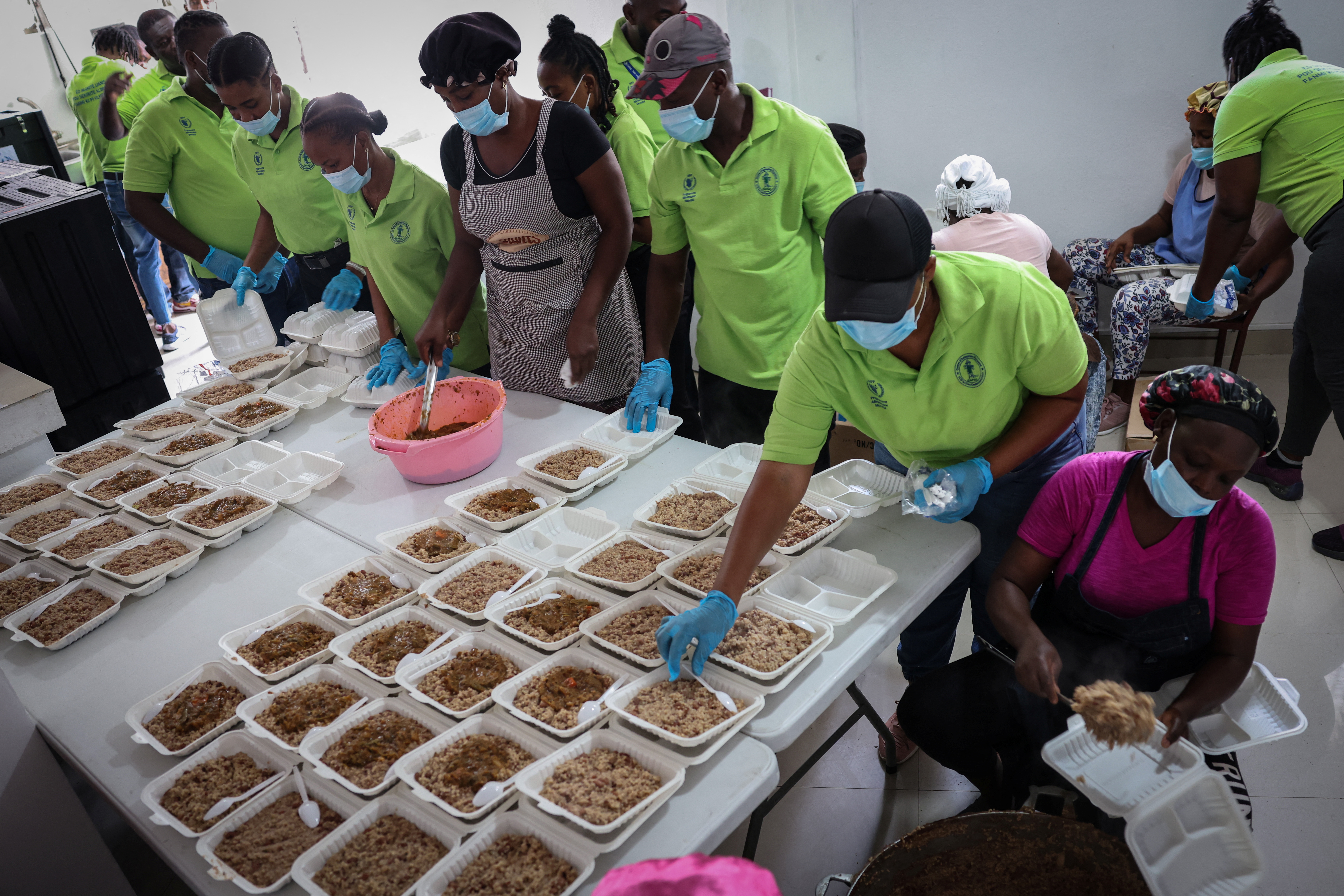 Volunteers in matching T-shirts at a community center prepare takeout trays of food