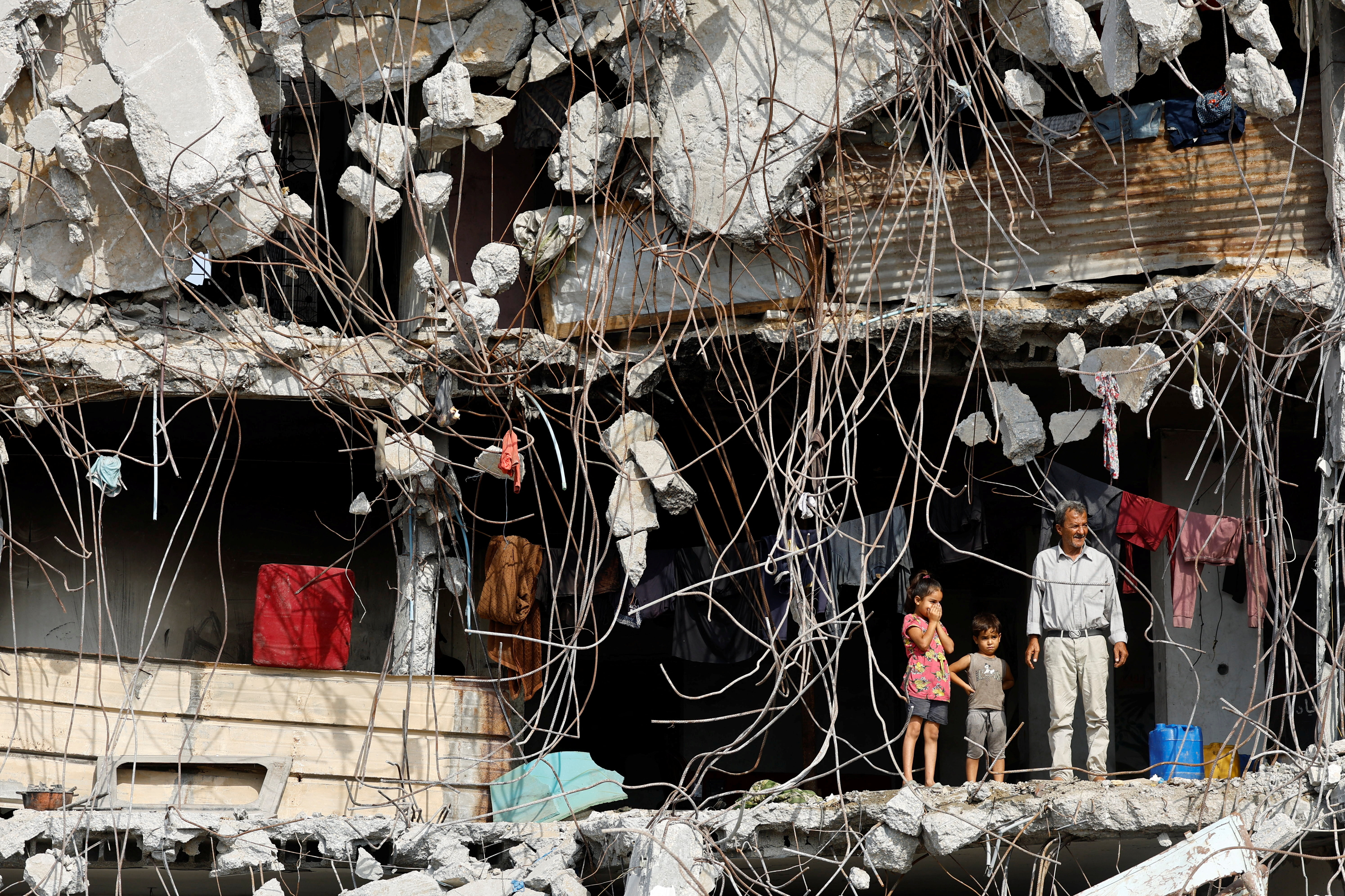 A Palestinian man and children stand at a heavily damaged building