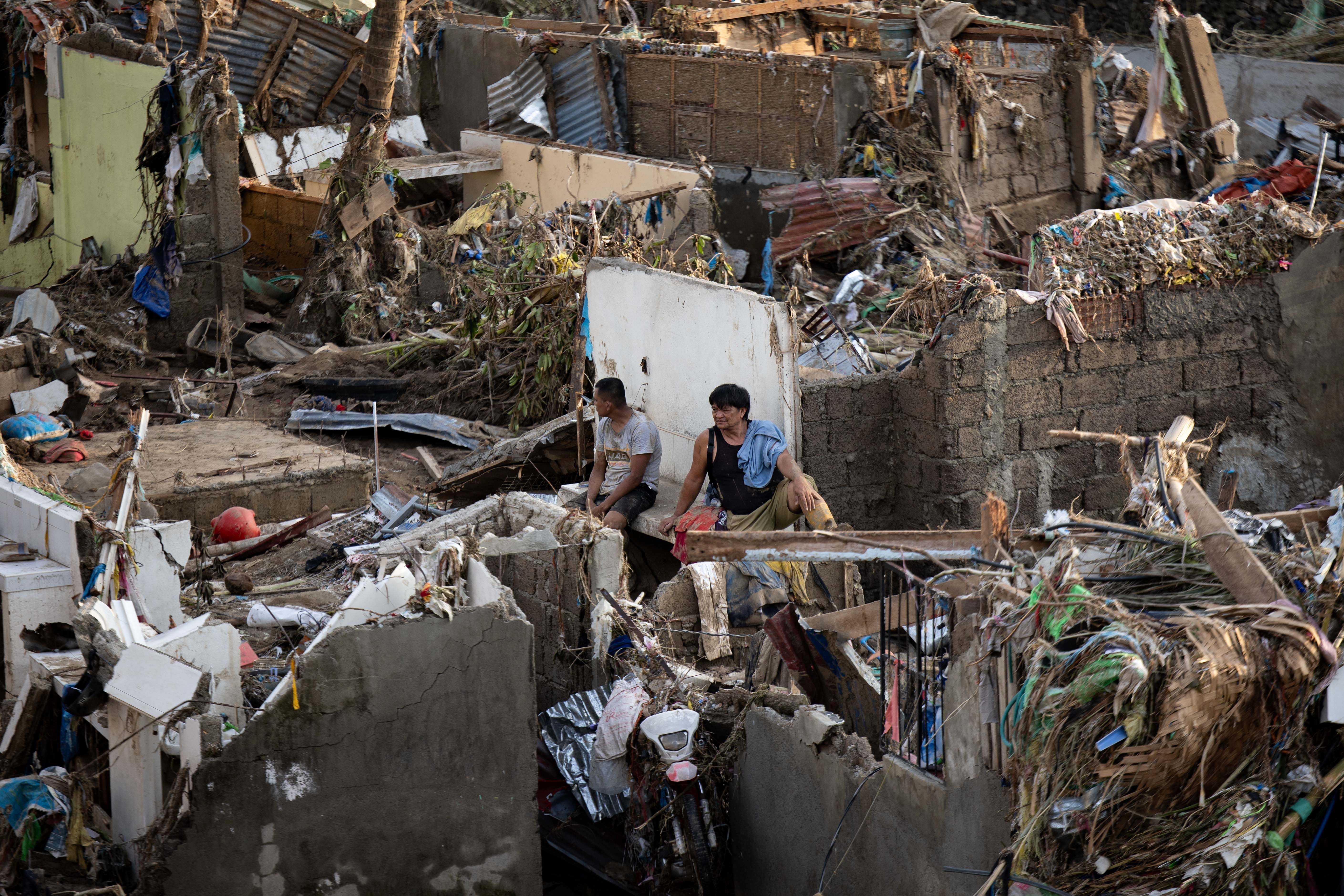 Men sit amid the remains of destroyed houses.
