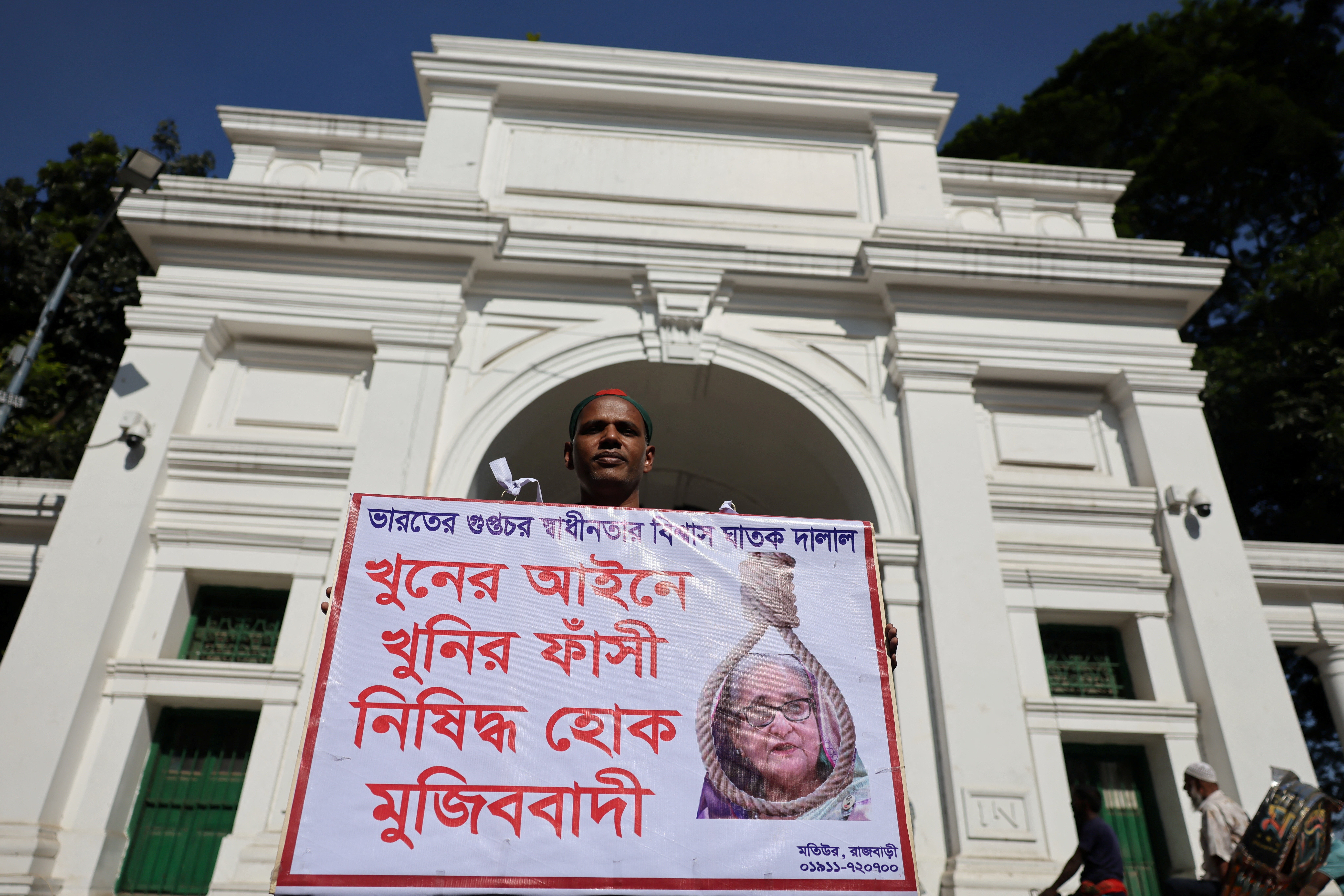 A man holds a poster in front of the court demanding the capital punishment ahead of the verdict on charges of crimes against humanity for a deadly crackdown on student-led protests in 2024 against the ousted Prime Minister Sheikh Hasina, in Dhaka, Bangladesh, November 17, 2025.