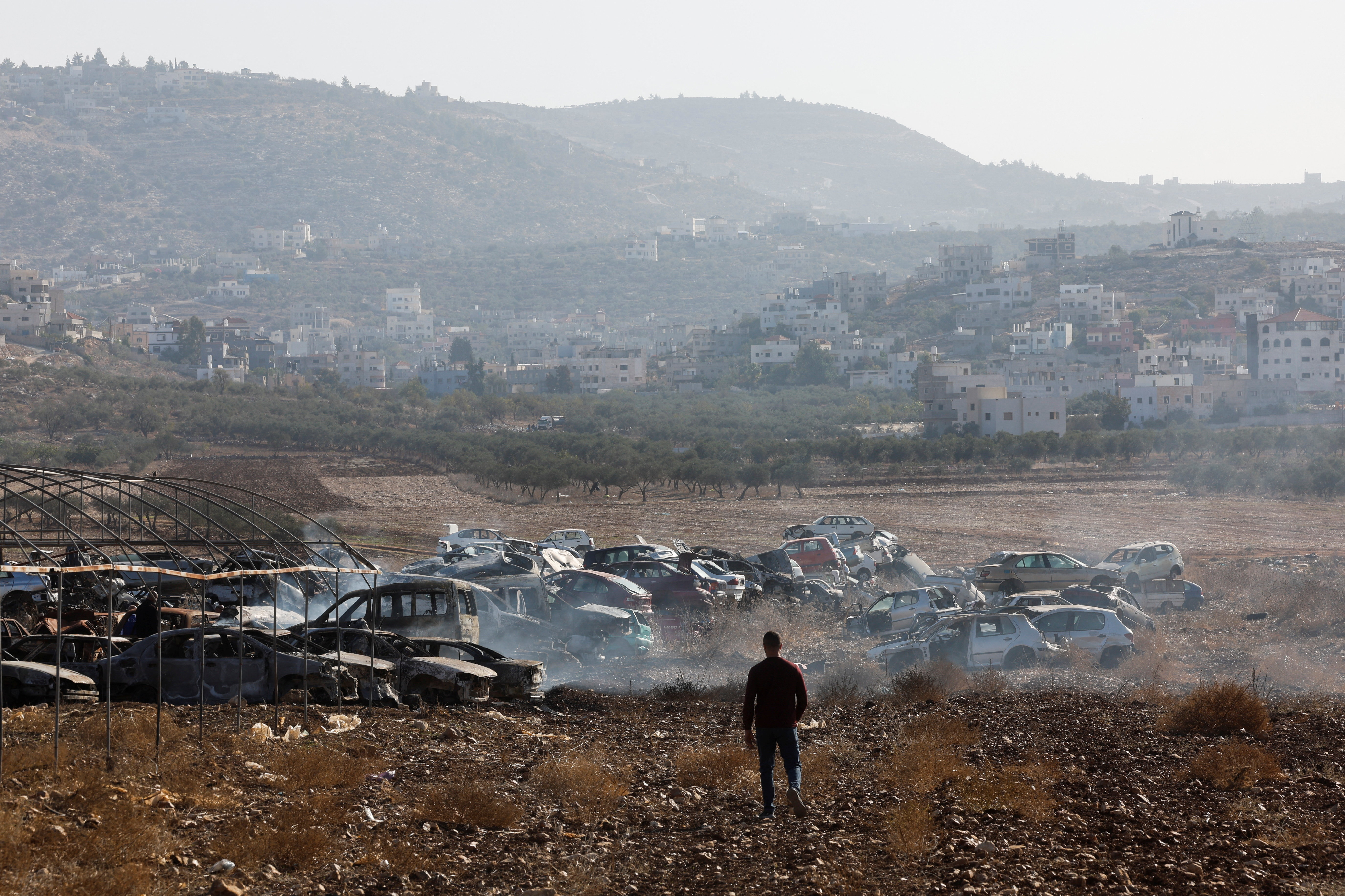 A Palestinian, Yahya Dalal, 32, walks near cars burnt in an attack by Israeli settlers, in Huwara in the Israeli-occupied West Bank, November 21, 2025. REUTERS/Ammar Awad