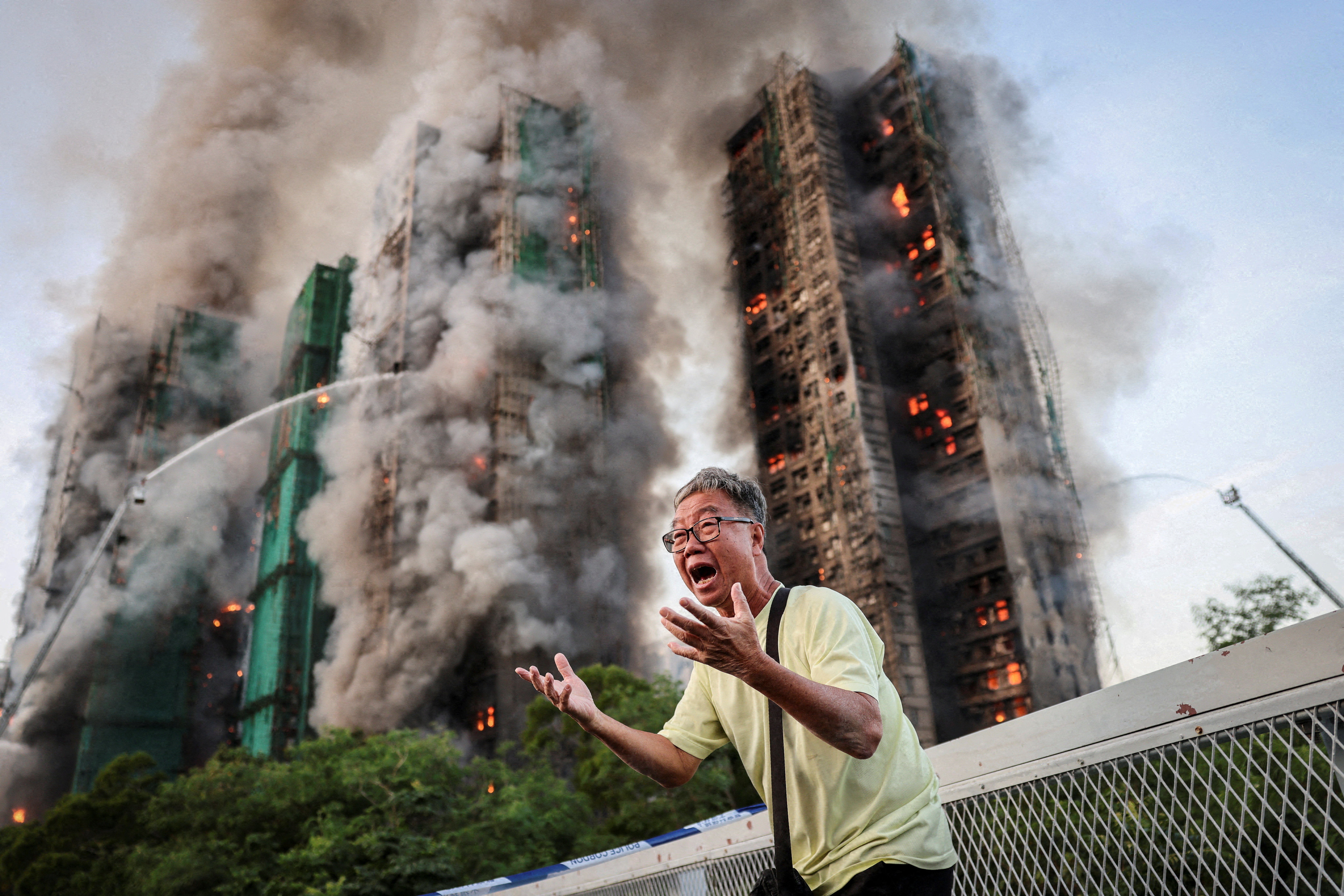 A man reacts in deep distress, with fire and smoke engulfing a tall tower behind him.