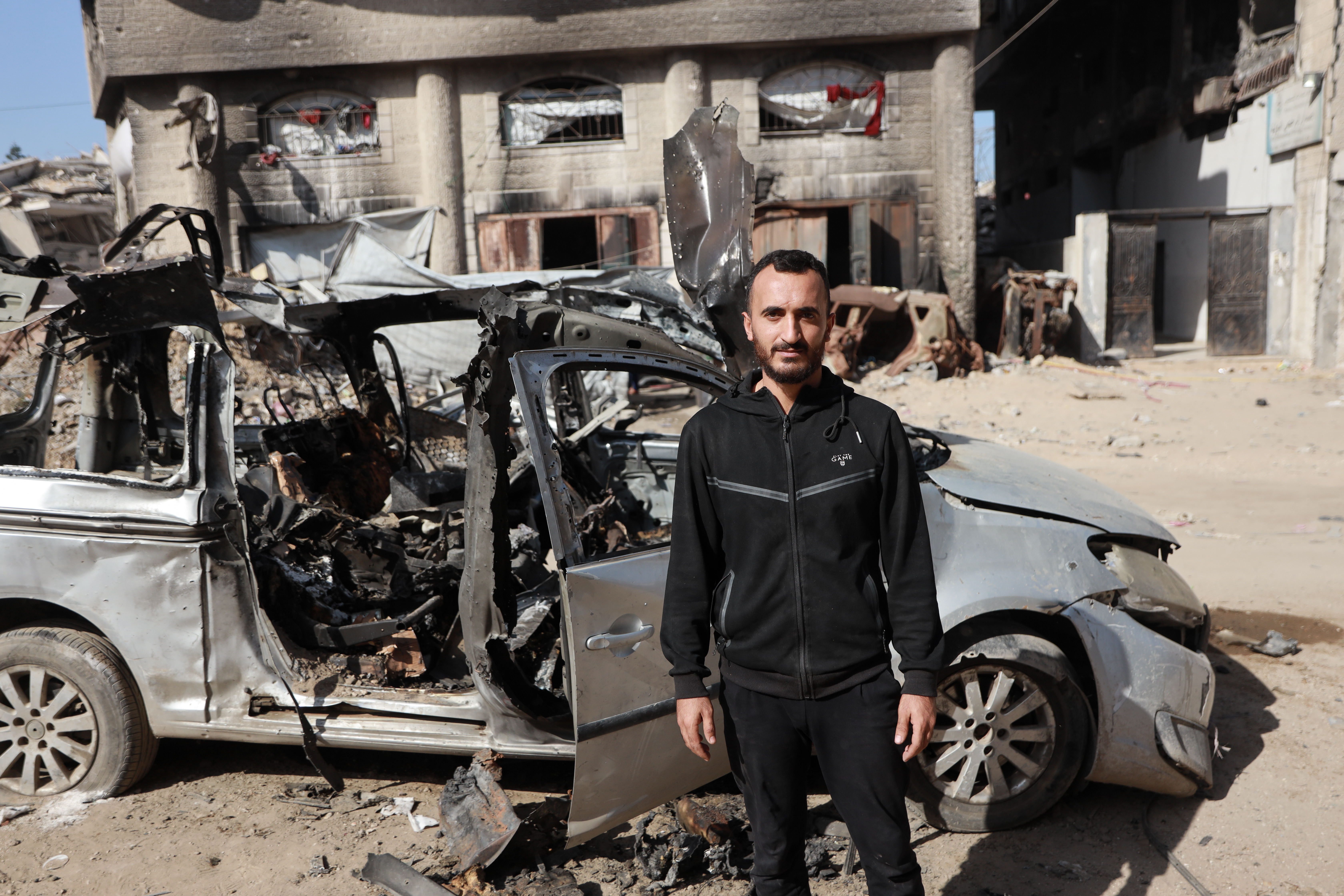 A man stands in front of a destroyed car