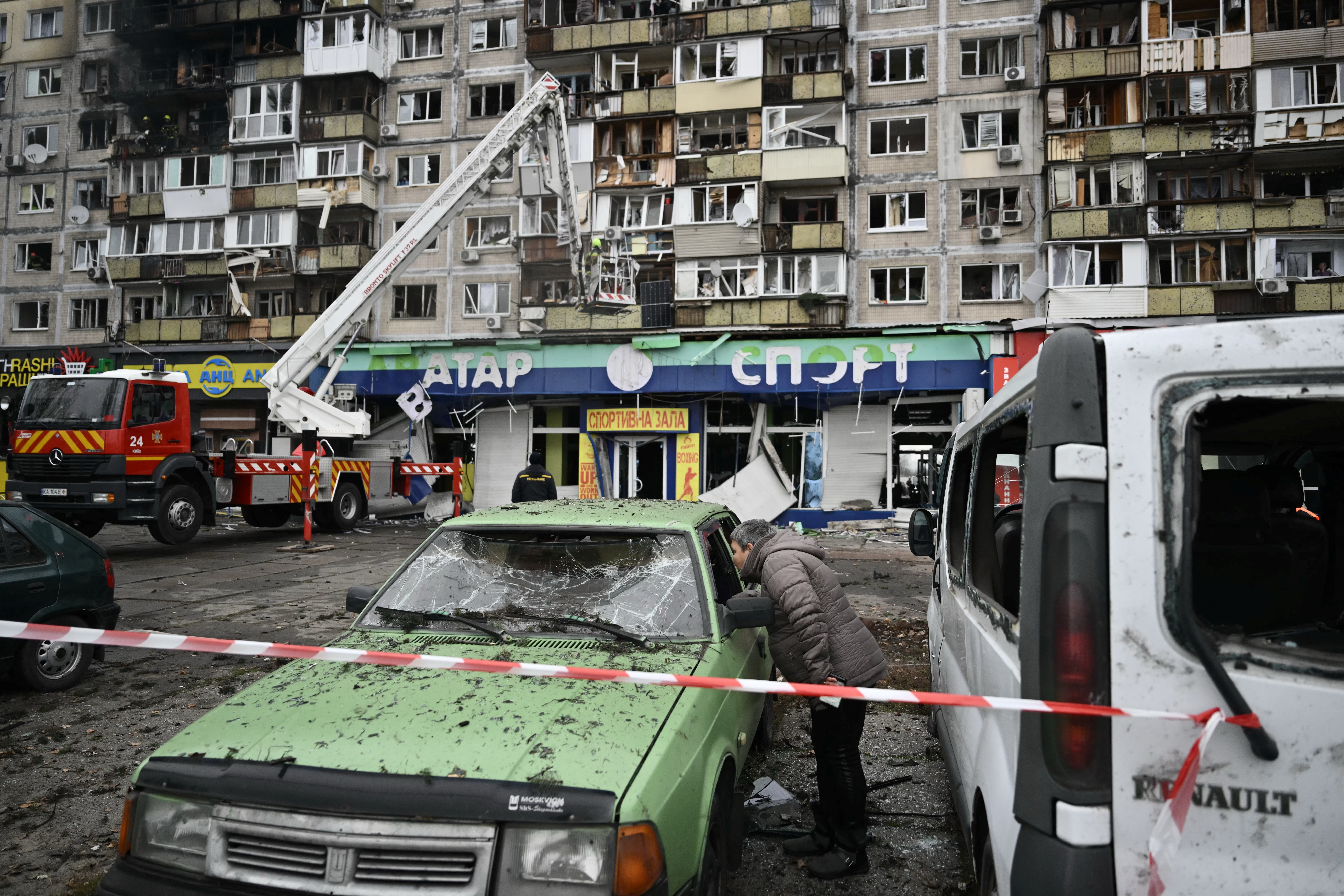 A local resident inspects a damaged car in front of a damaged residential building following an air attack in Kyiv