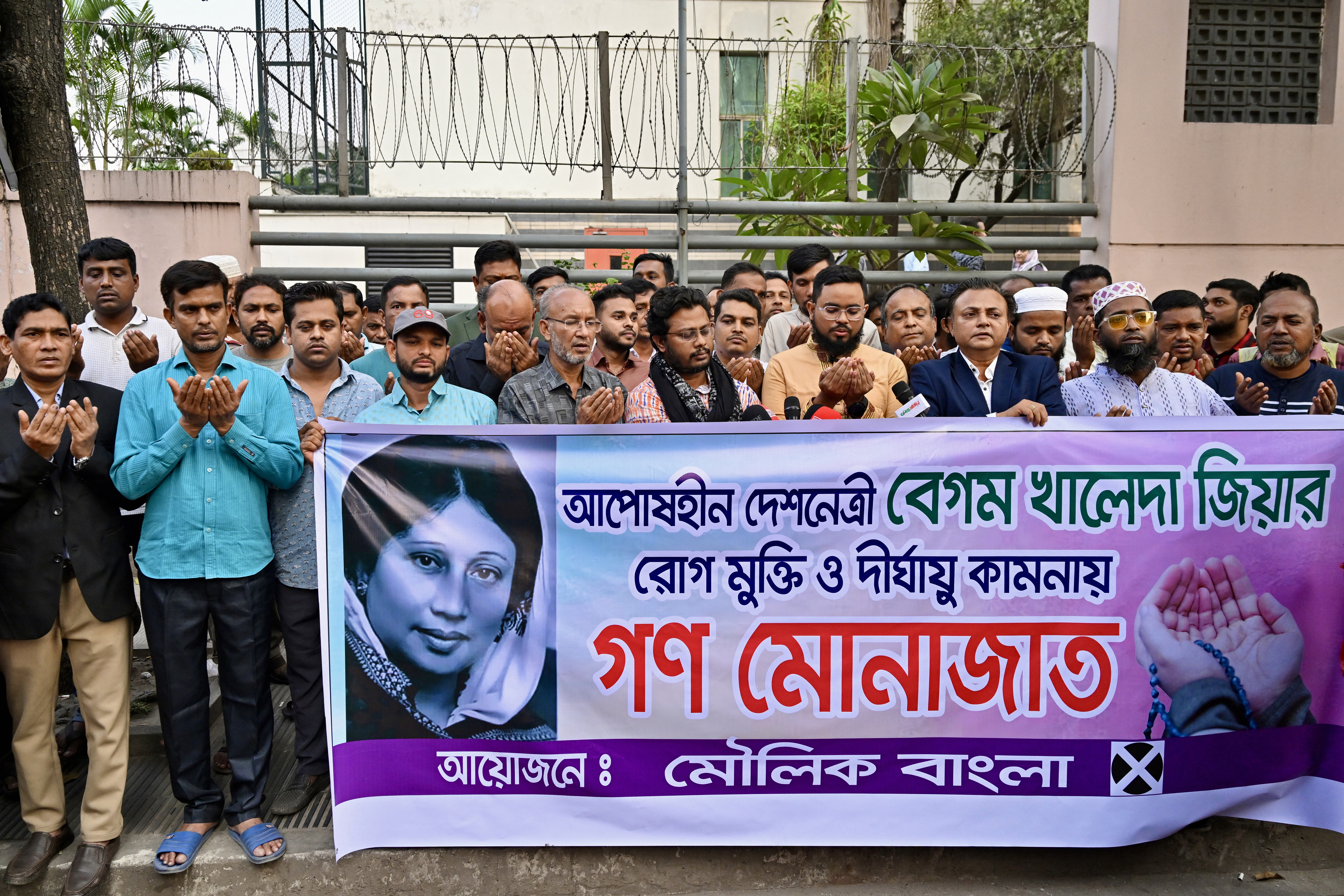Activists in support of Bangladesh's former prime minister Khaleda Zia, hold a banner with her portrait as they pray for her recovery in front of the Evercare Hospital in Dhaka on November 29, 2025.