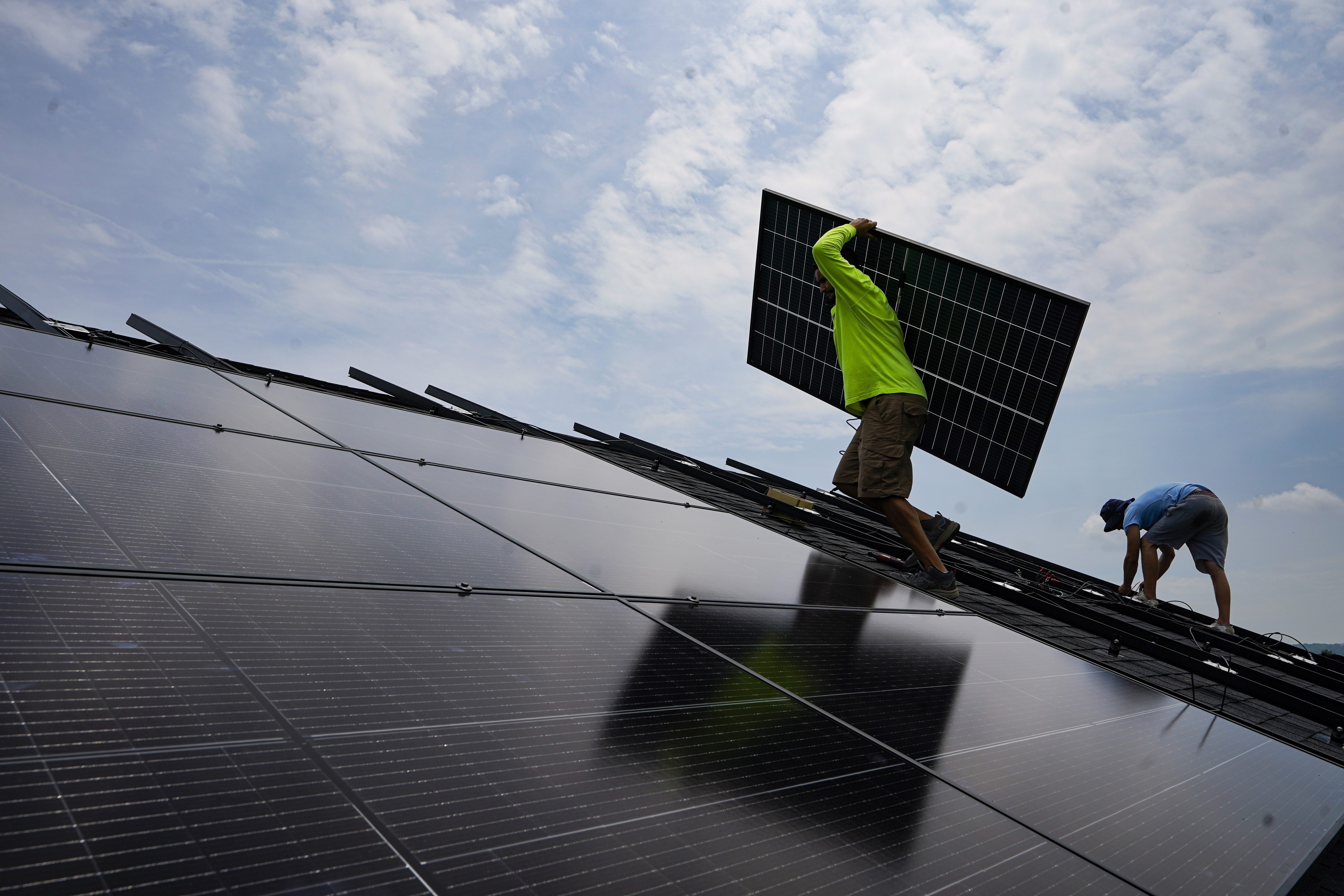 Nicholas Hartnett, owner of Pure Power Solar, carries a panel as he and Brian Hoeppner, right, install a solar array on the roof of a home in Frankfort, Kentucky, US