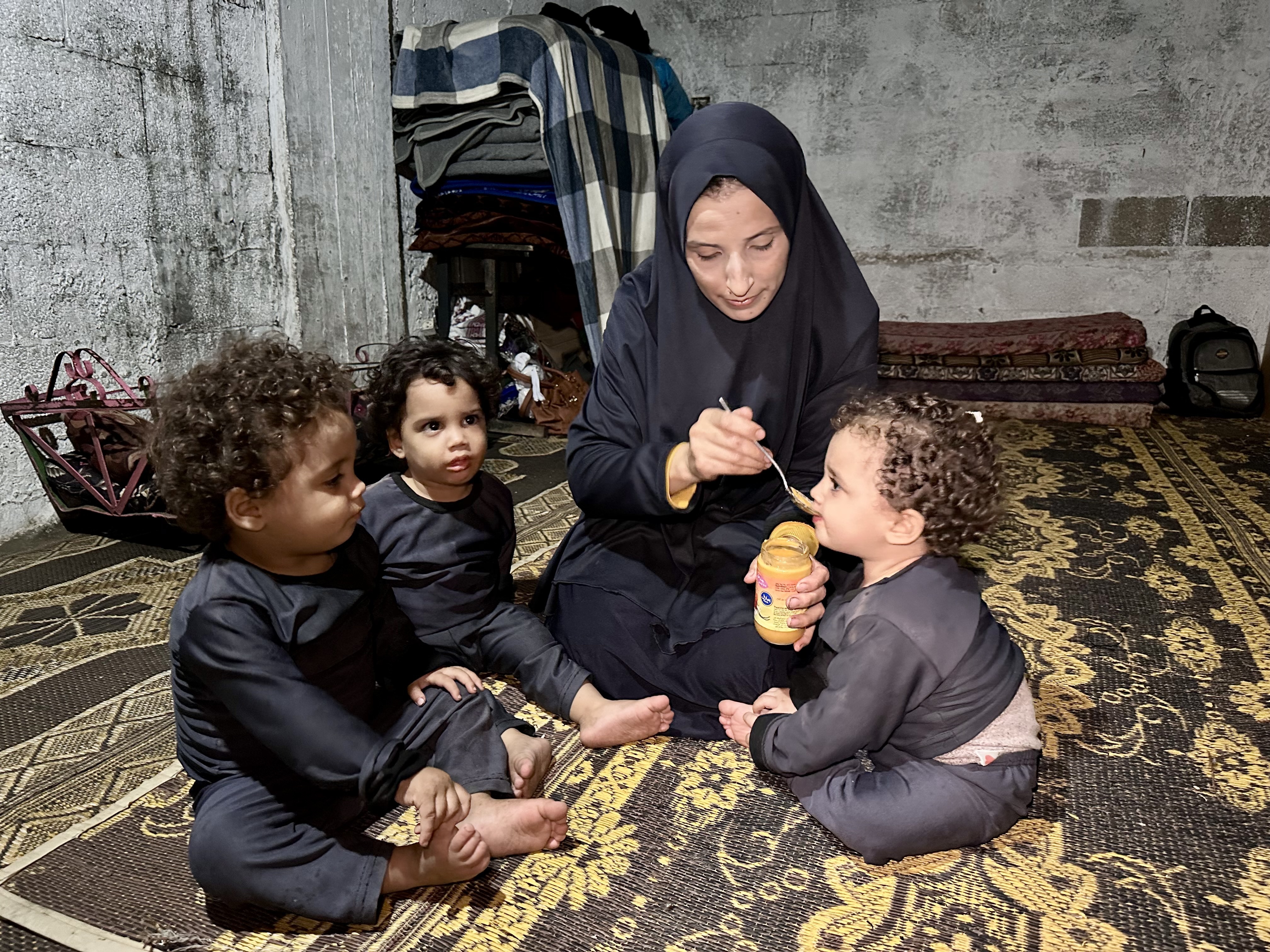 Israa feeding the triplets on a worn plastic mat on the floor