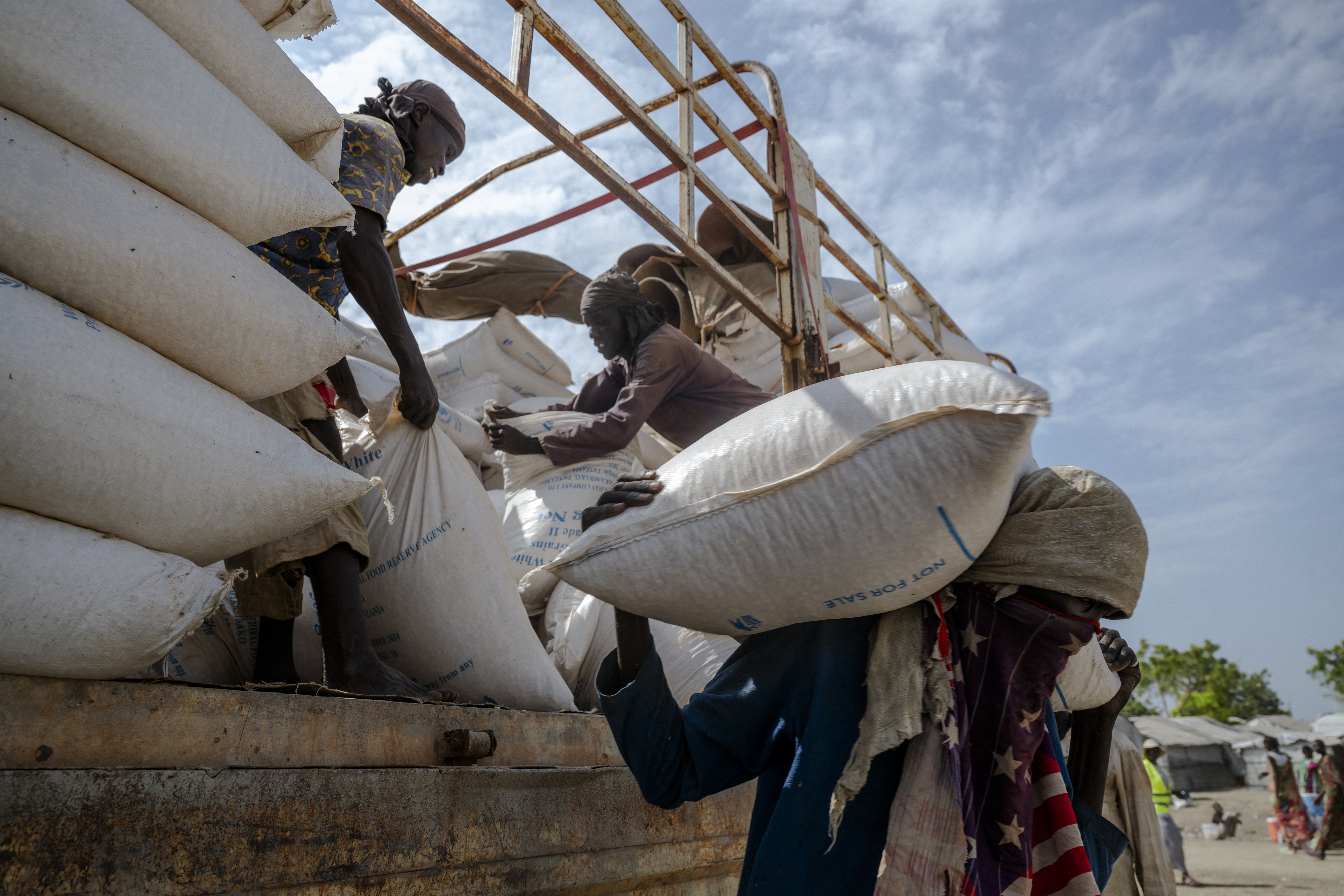 Workers unload a World Food Programme (WFP) supply truck at a distribution center in the Bentiu internally displaced persons camp, Unity State, South Sudan, on November 6, 2025. The camp, home to over 119,000 people, relies on such deliveries to provide food and essential supplies to residents amid flooding and ongoing global aid cuts. (Photo by Rian COPE / AFP)