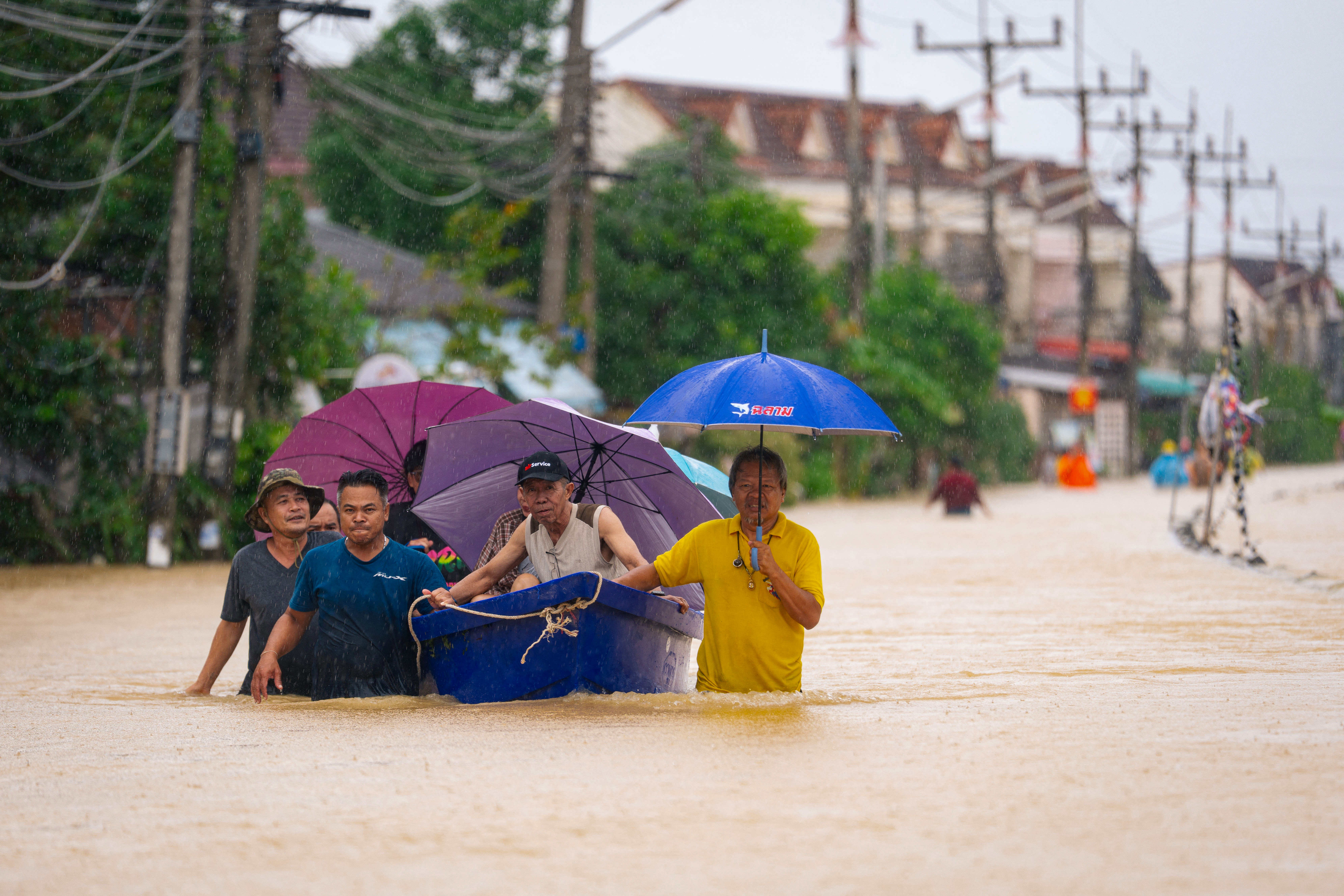 People wade through flood waters with residents being evacuated on a boat in Hat Yai in Thailand's southern Songkhla province on November 25, 2025, as severe flooding affected thousands of people in the country's south following days of heavy rain. (Photo by Arnun Chonmahatrakool / THAI NEWS PIX / AFP)