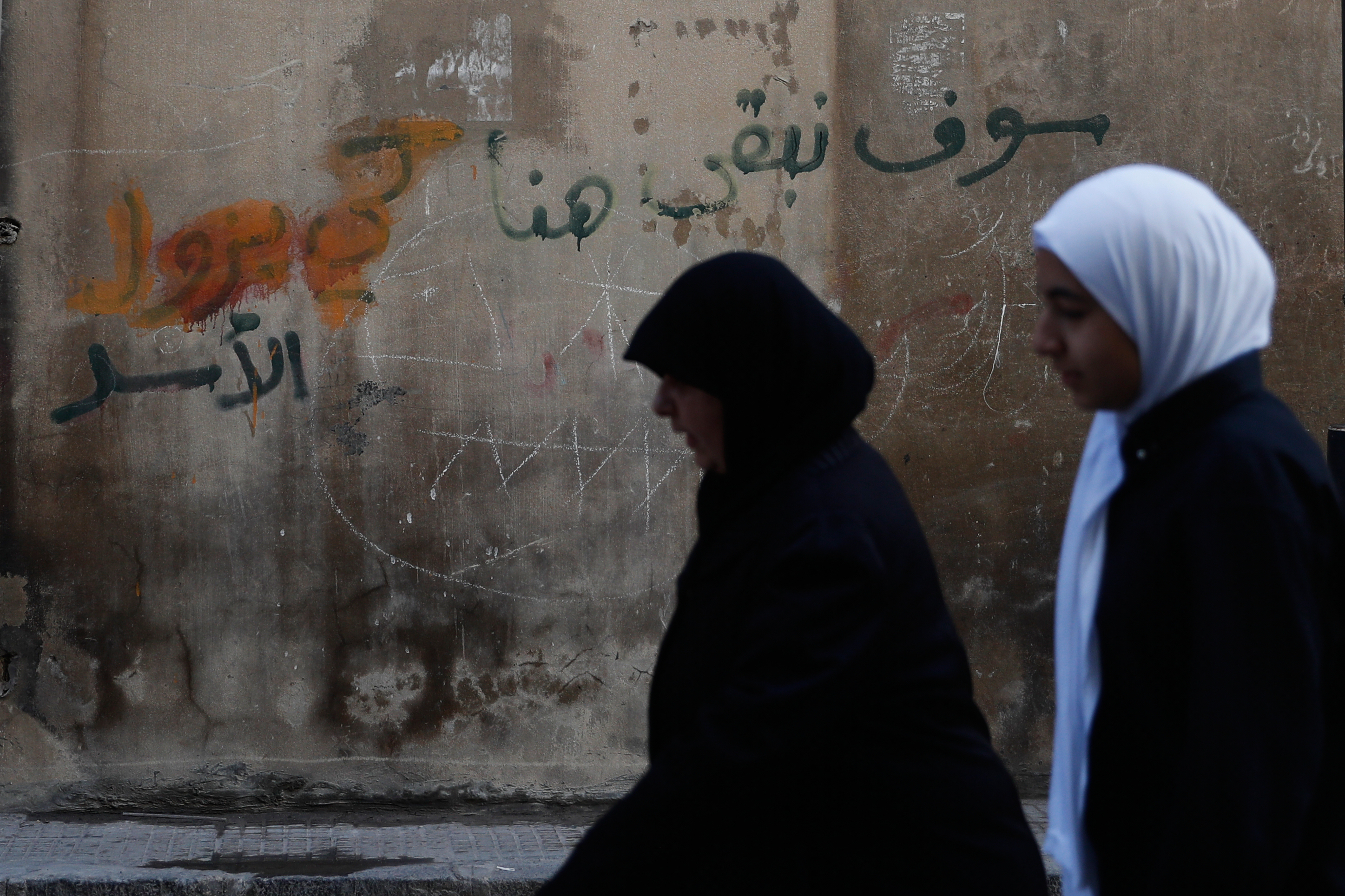 Women walk past a wall with a graffiti reading in Arabic "We will remain here, Assad" in the city of Homs, Syria, Friday, Nov. 21, 2025. (AP Photo/Omar Sanadiki)