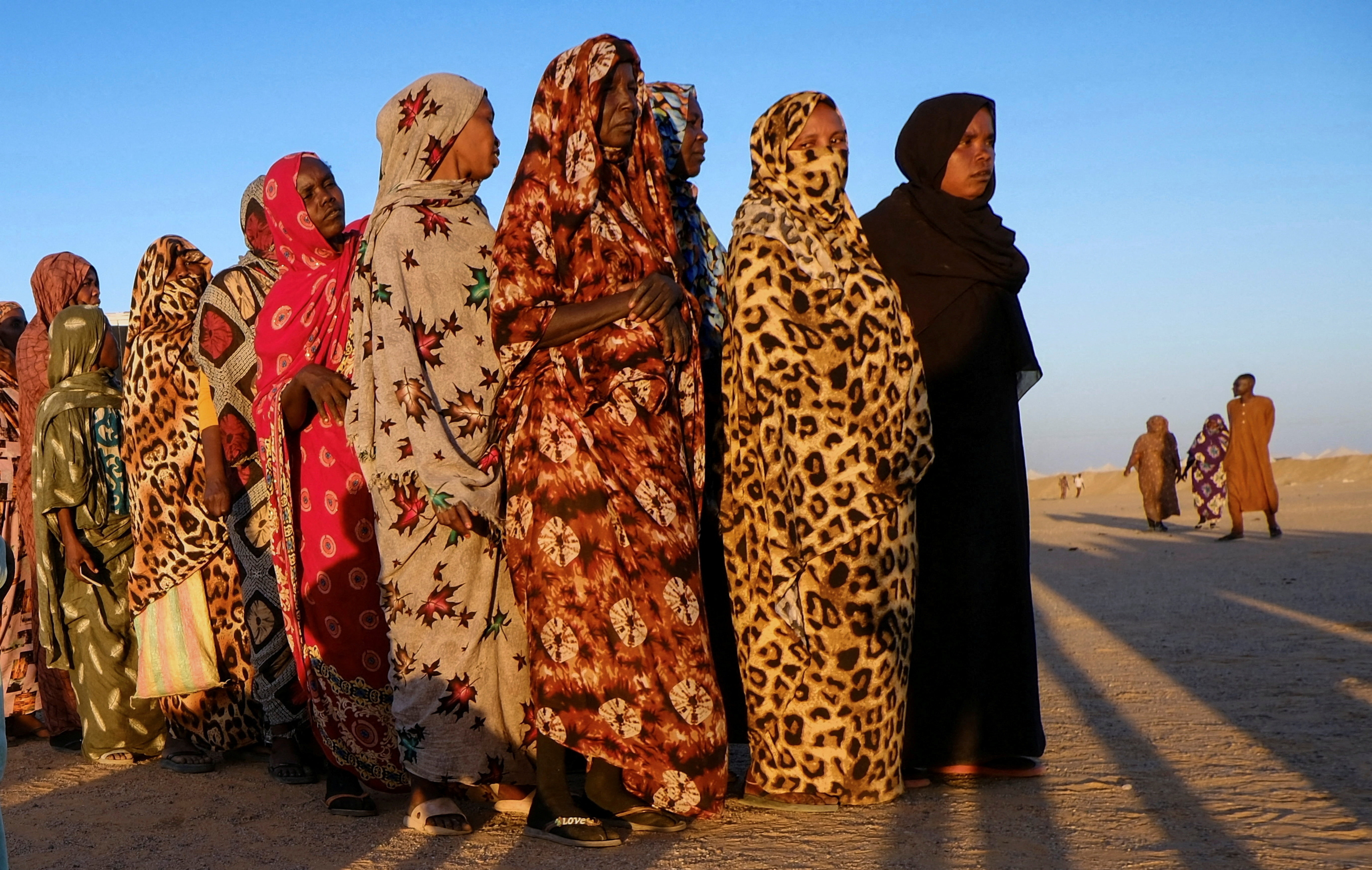 Displaced women stand in line as they wait for their turn to receive aid, at a displacement camp.