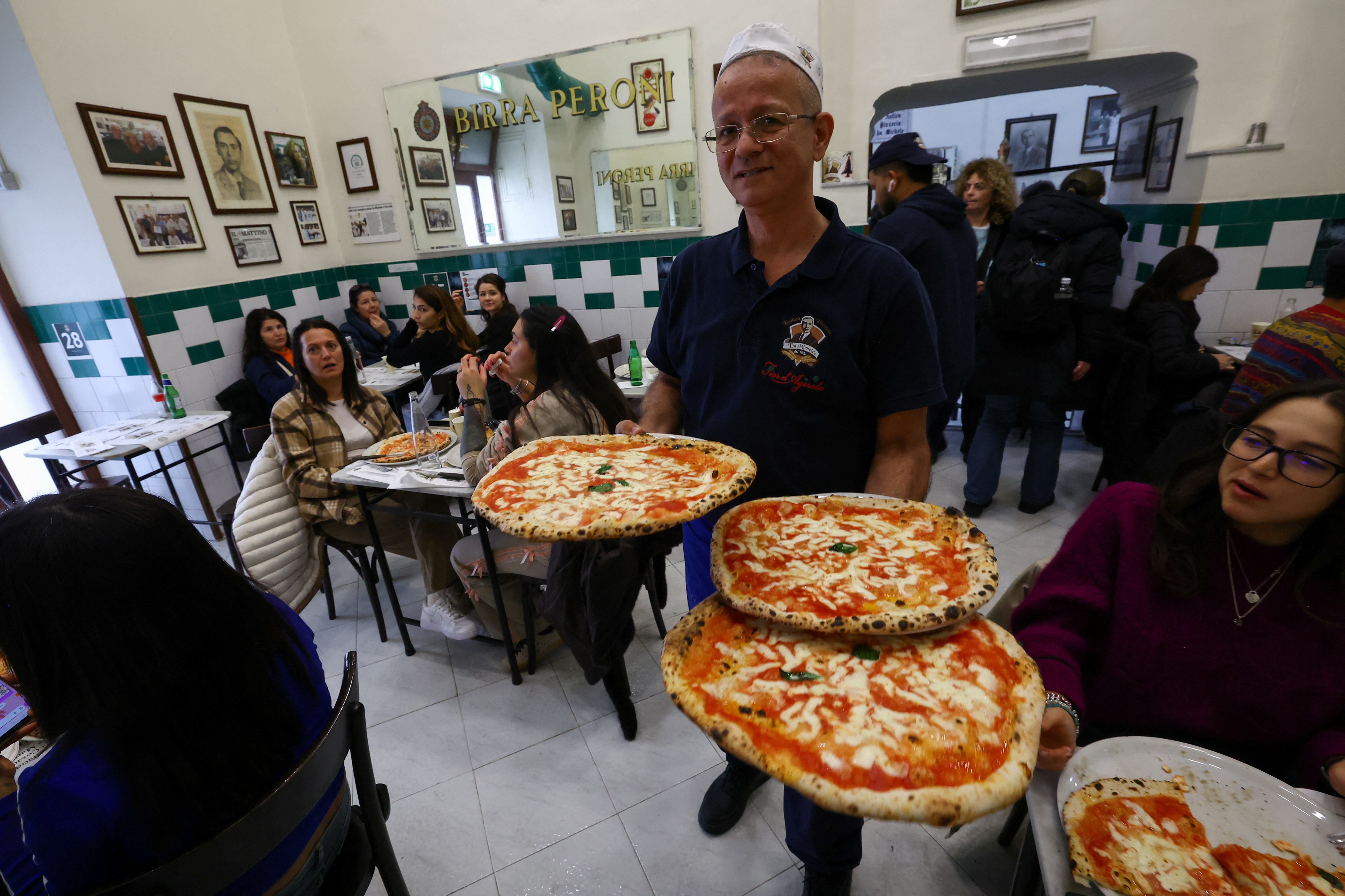 A waiter carries pizzas at L'antica Pizzeria da Michele as Italian cuisine awaits a crucial UNESCO decision that could recognise it as an Intangible Cultural Heritage of Humanity in Naples, Italy, December 5, 2025. REUTERS/Ciro De Luca