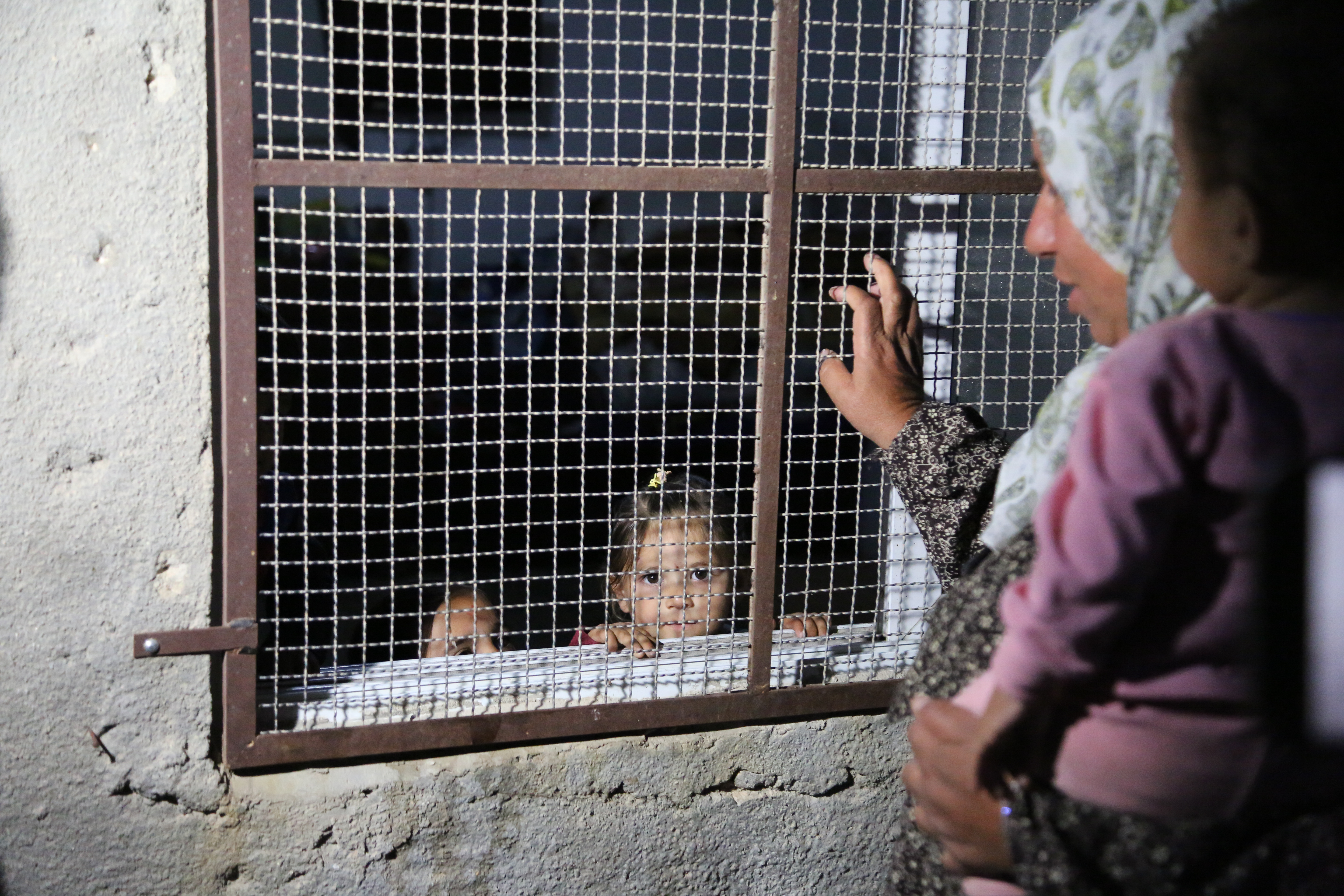 Hamida Hamamda in her yard with her grandchilren. One of her granddaughters stands in the house, behind the metal grates they had to install to try to protect themselves froms settlers