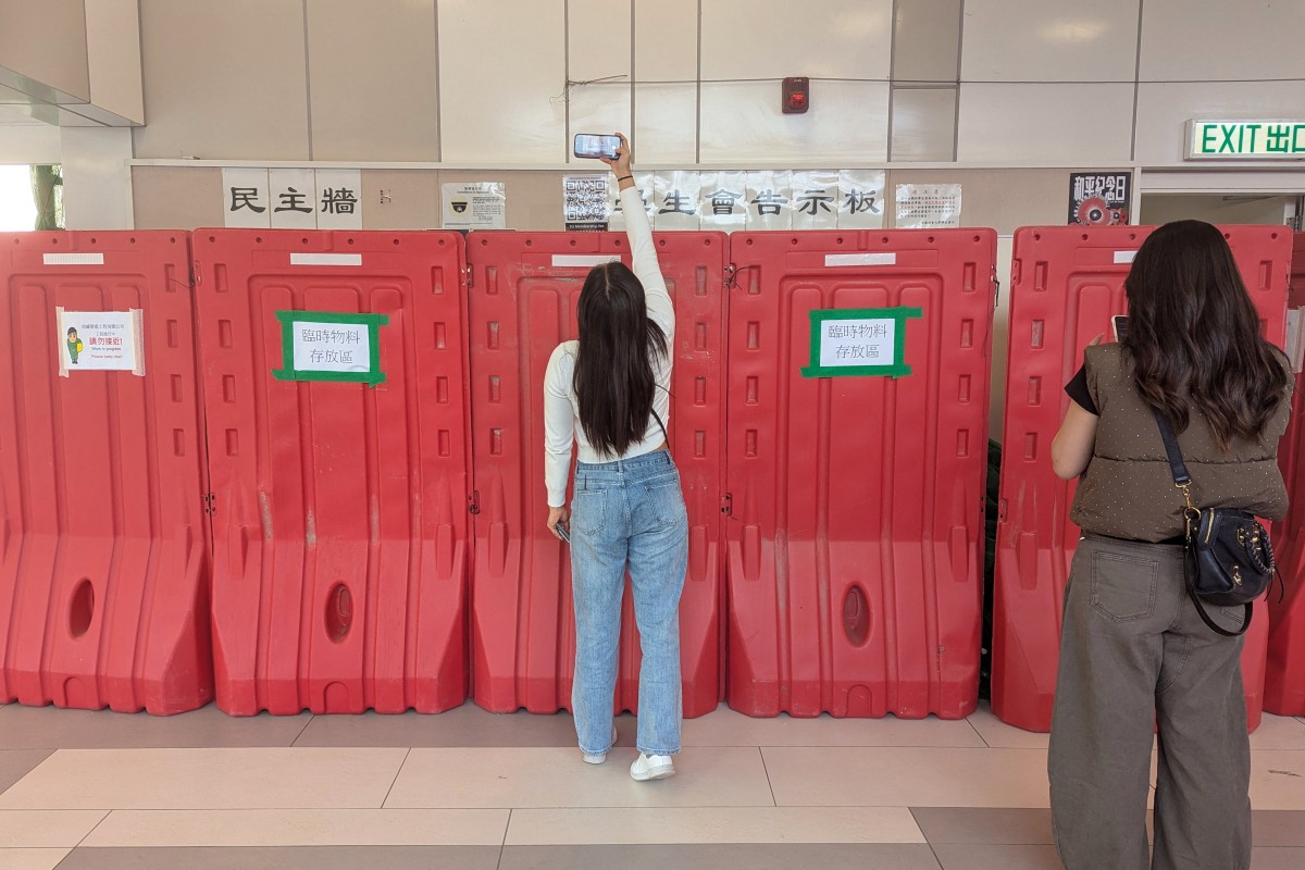 A woman takes a photo with her phone above barricades in front of the student union-run notice board.