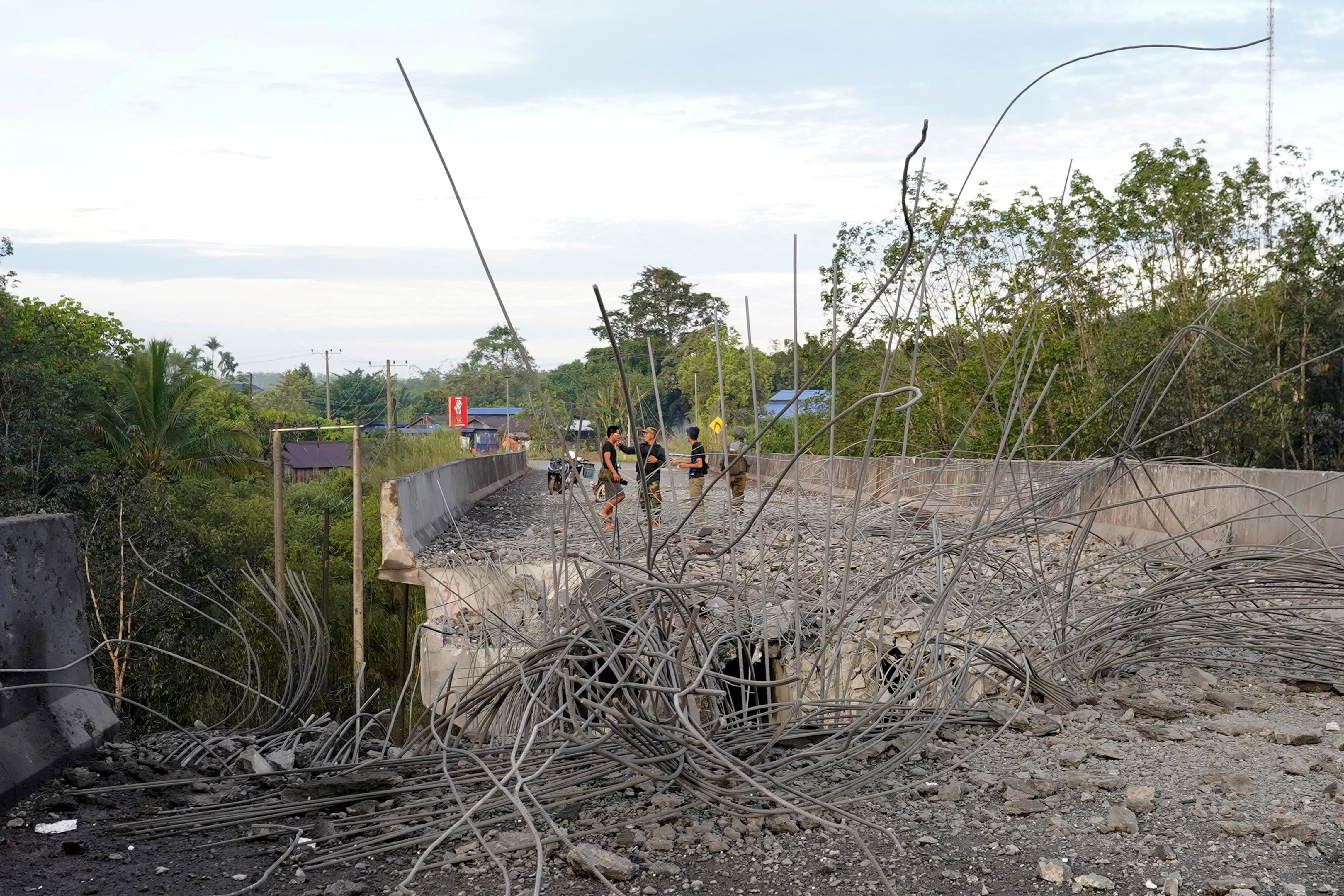 People stand on a damaged bridge in Pursat in Pursat province on December 13, 2025, amid clashes along the Cambodia-Thailand border. The latest clashes between the Southeast Asian neighbours, which stem from a long-running dispute over the colonial-era demarcation of their 800-kilometre (500-mile) frontier, have displaced around half a million on both sides. (Photo by AFP)