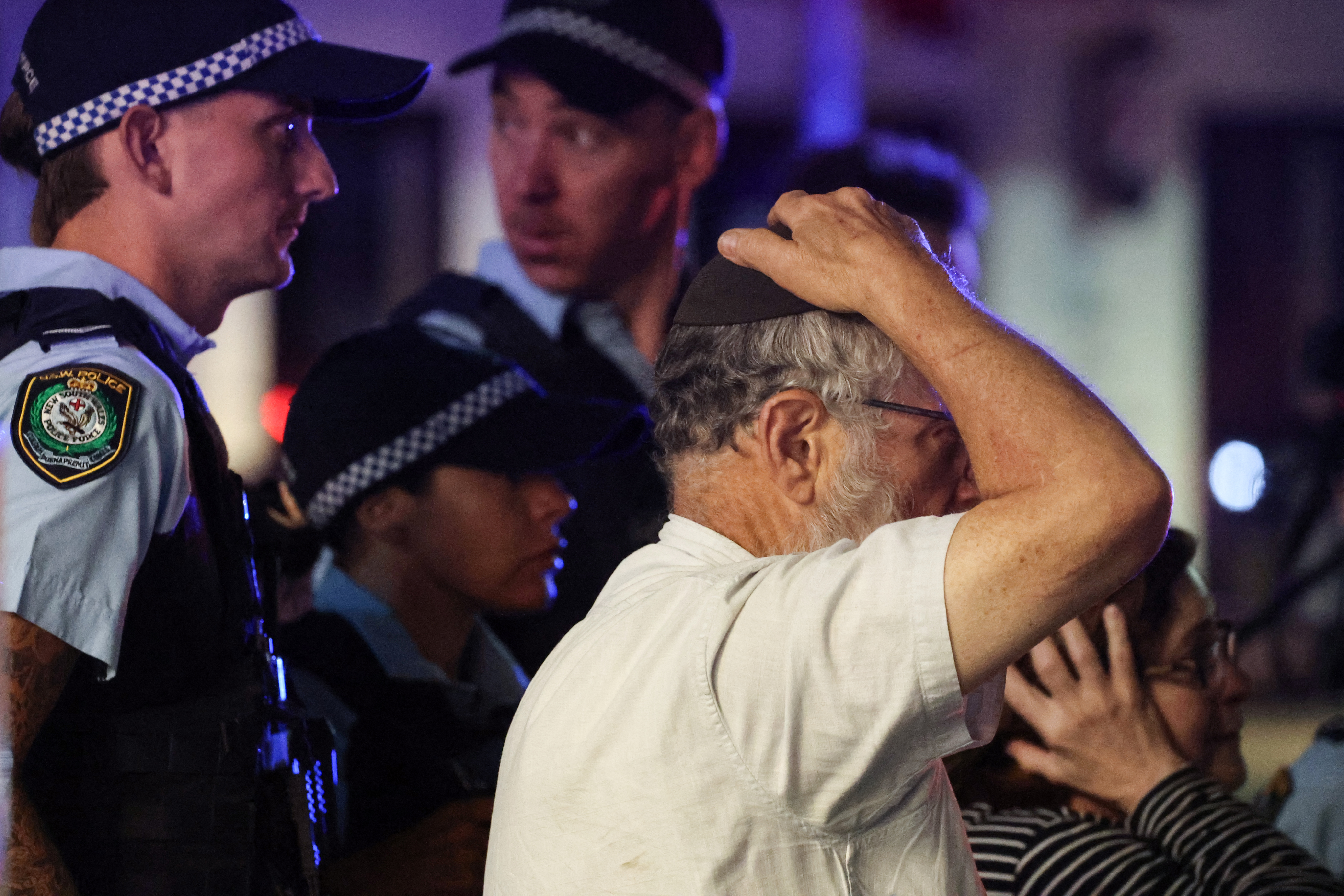 A member of the Jewish community reacts as he walks with police towards the scene of a shooting at Bondi Beach in Sydney on December 14, 2025. Australian police said two people were in custody following reports of multiple gunshots on December 14 at Sydney's famed Bondi Beach, urging the public to take shelter. (Photo by DAVID GRAY / AFP)