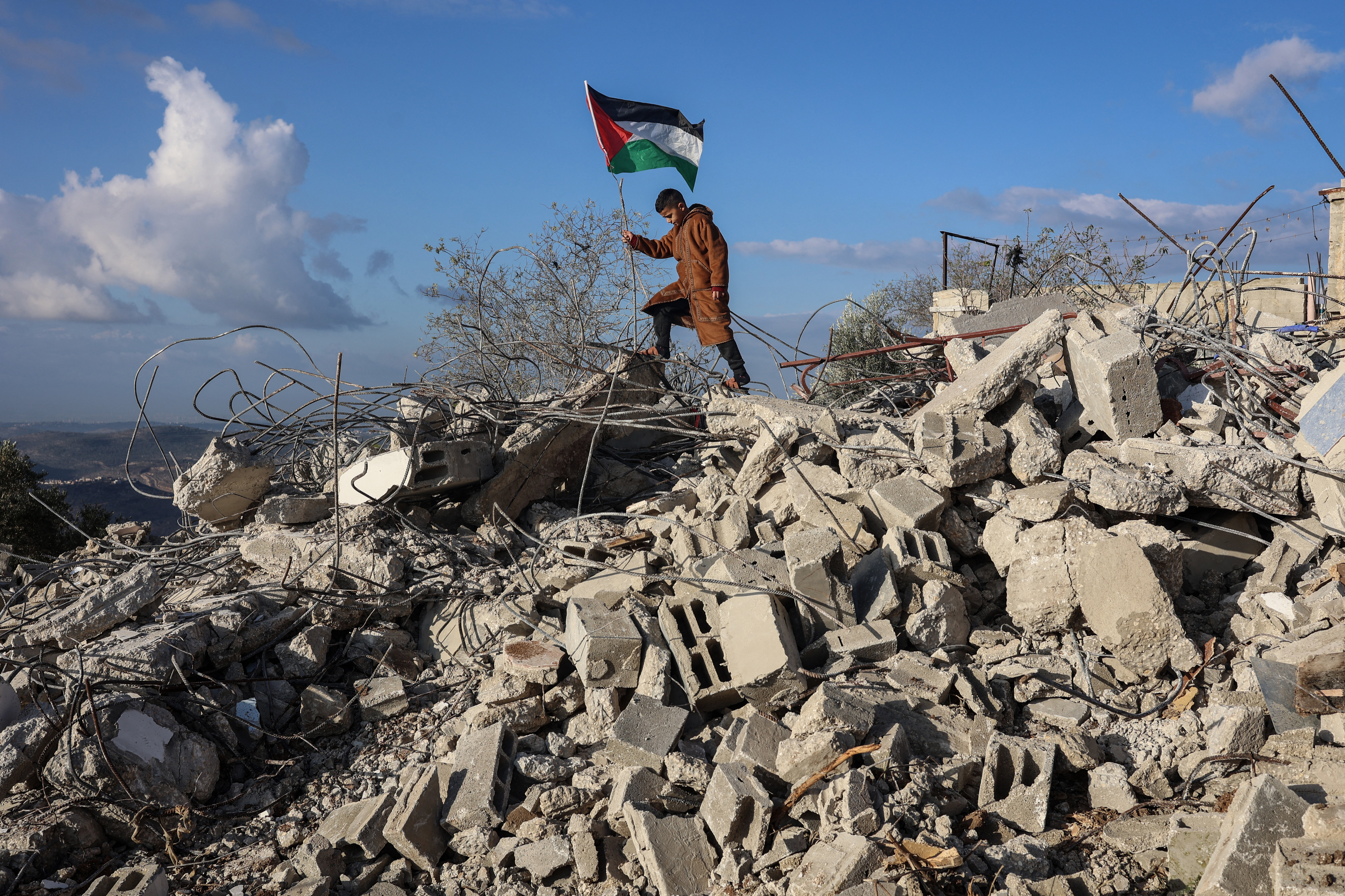 A boy poses for photos next to a Palestinian flag on the rubble of a house demolished by Israeli authorities.