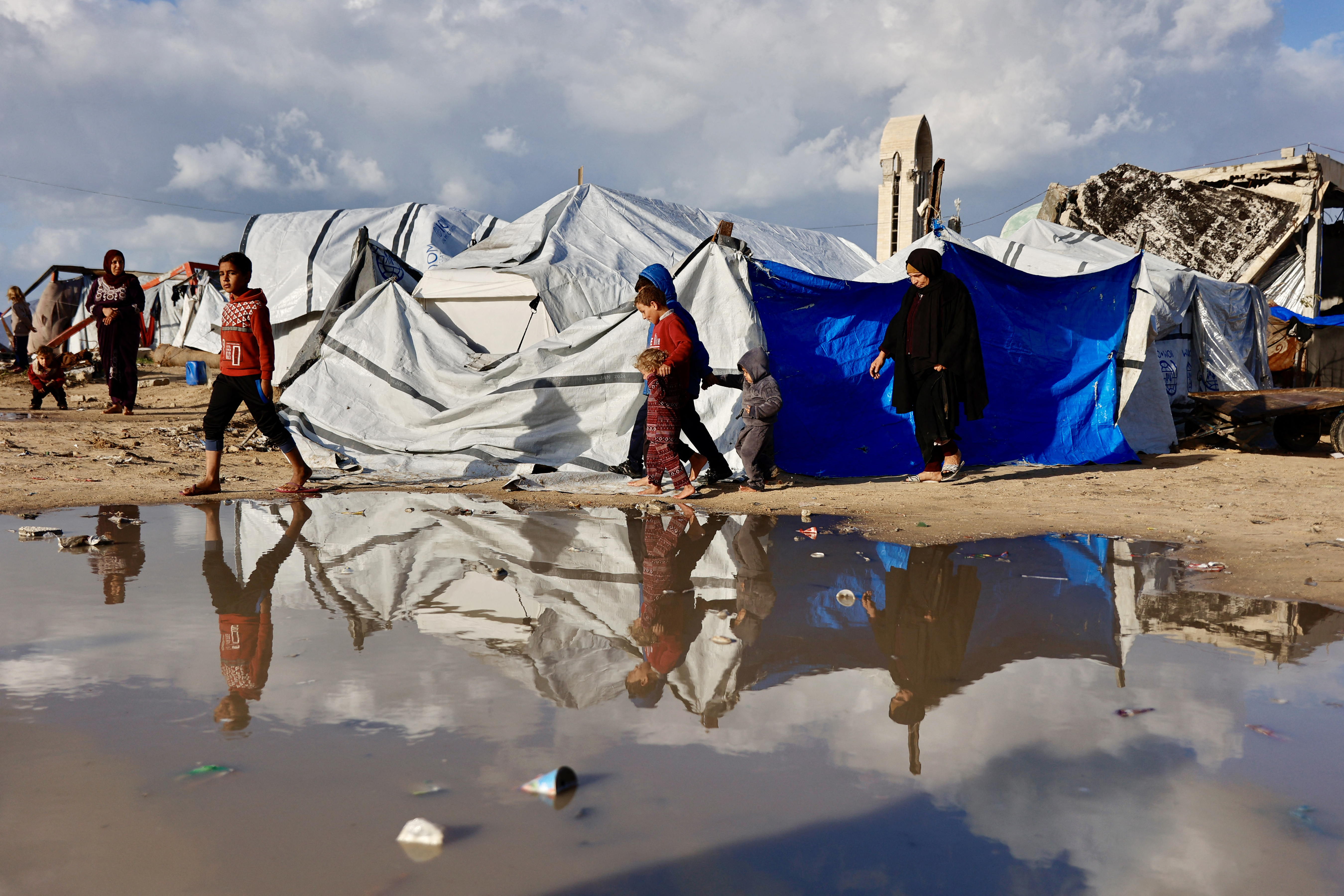Displaced Palestinians walk past a large pool of rain water accumulated near tent shelters as the region experiences rain and cold winter conditions, in Gaza City